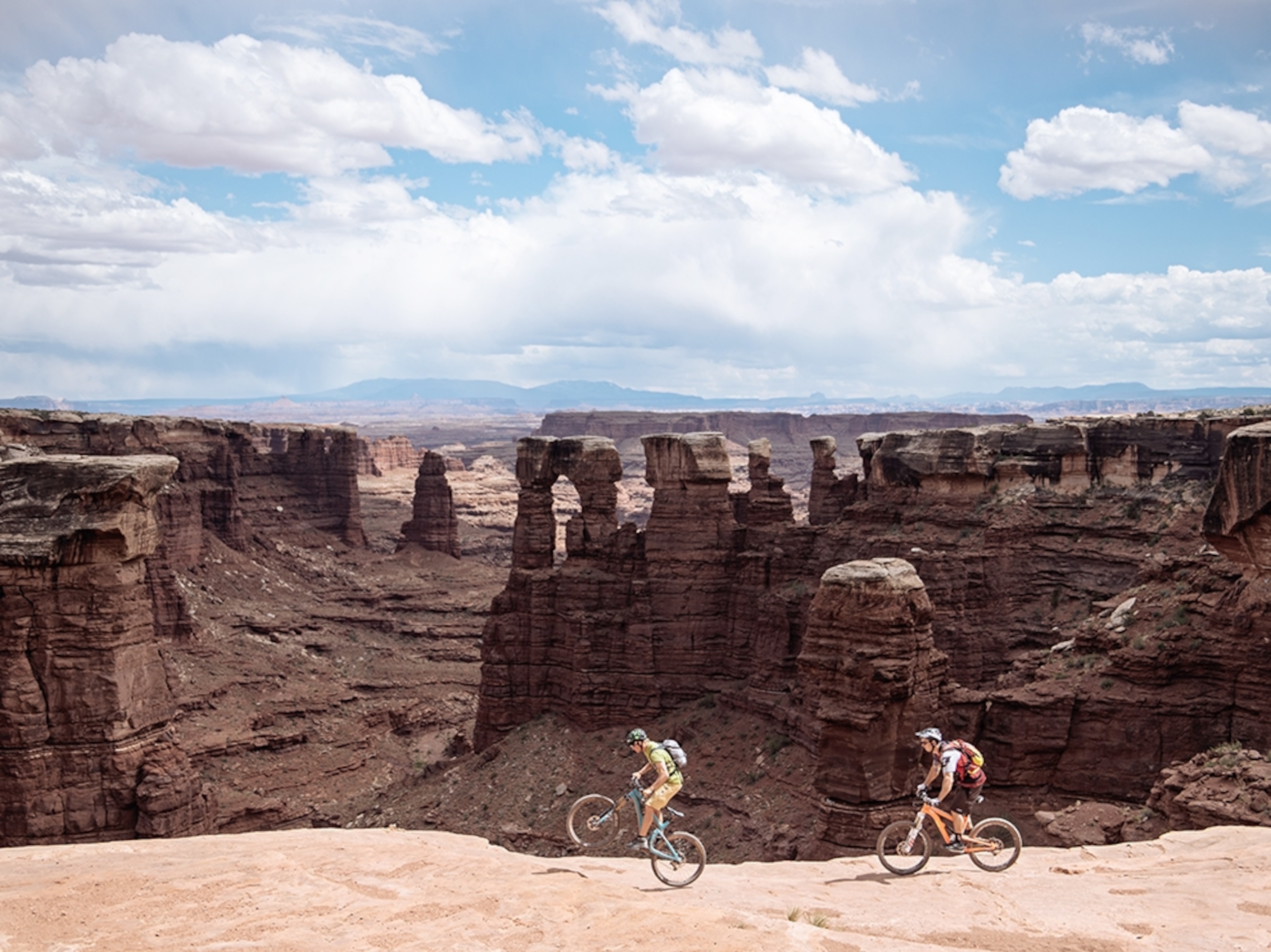 two mountain bikers riding along the edge of steep drop off in Utah.