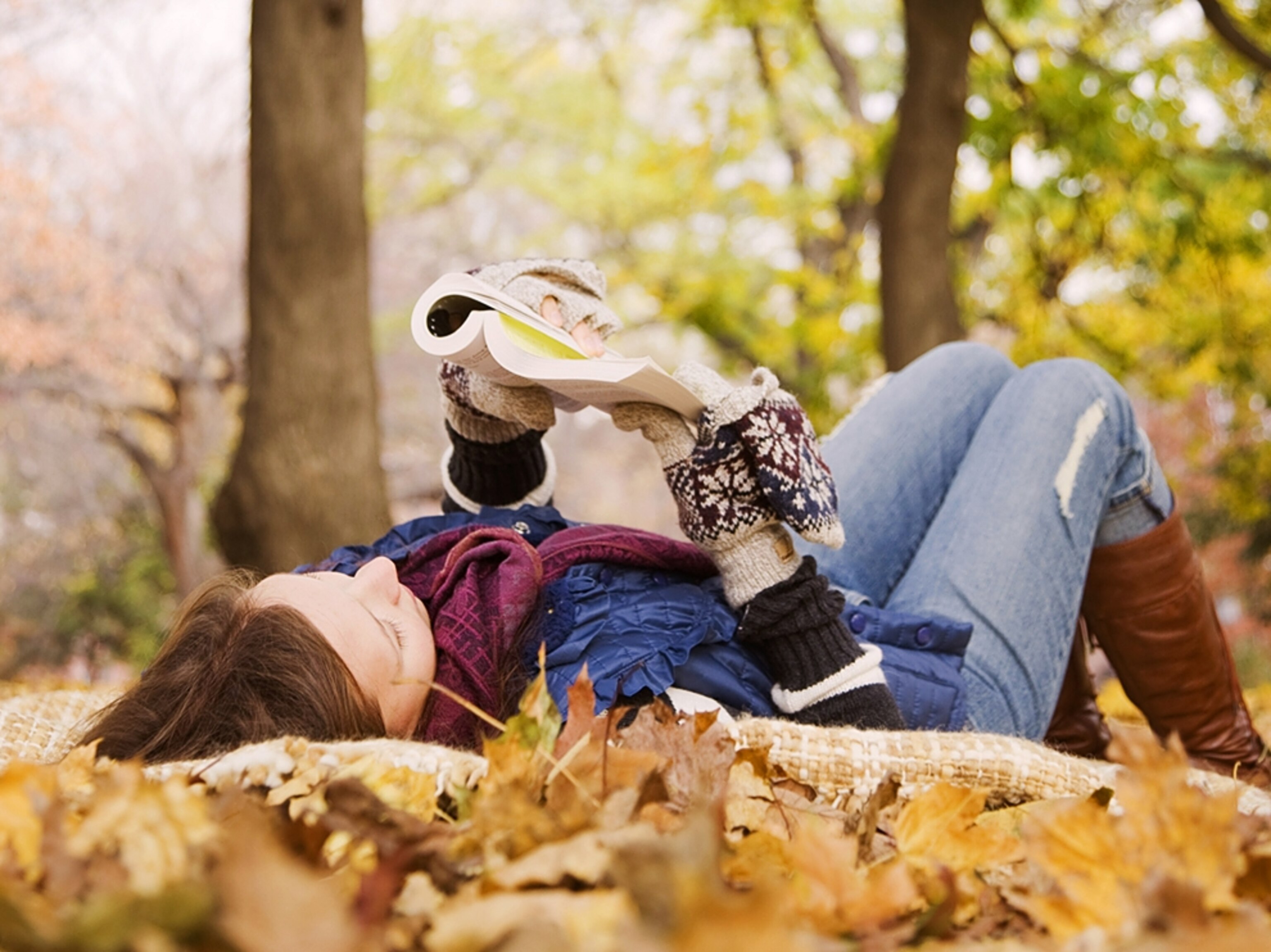 a woman reading a book in the park during autumn