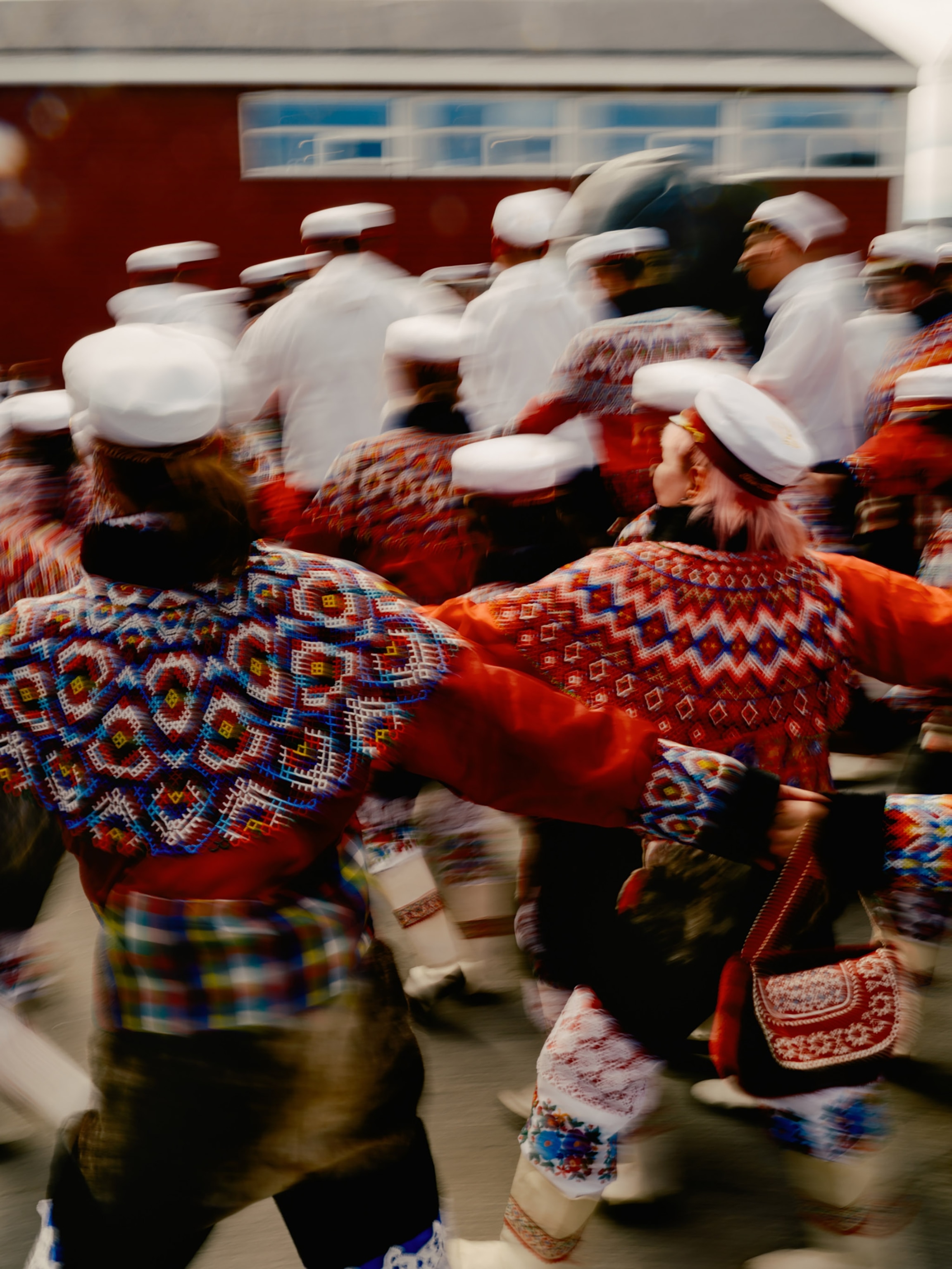 A blurry image of people wearing white captain's hats and traditional clothing dancing together.