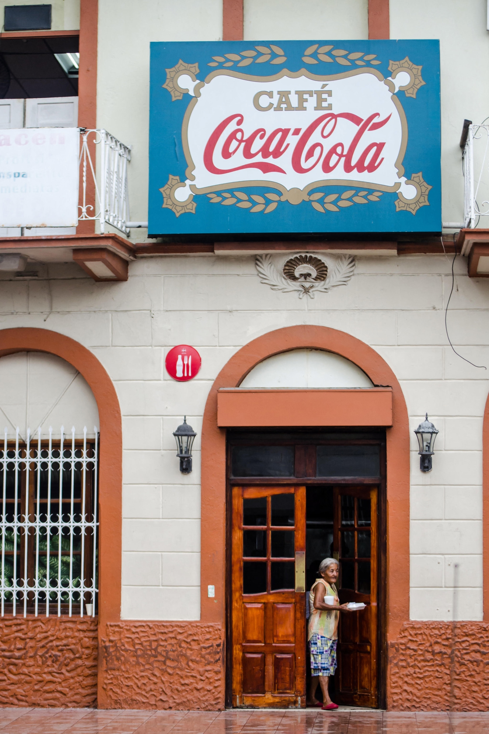 Woman stands outside building with sign saying 'Cafe Coca Cola'