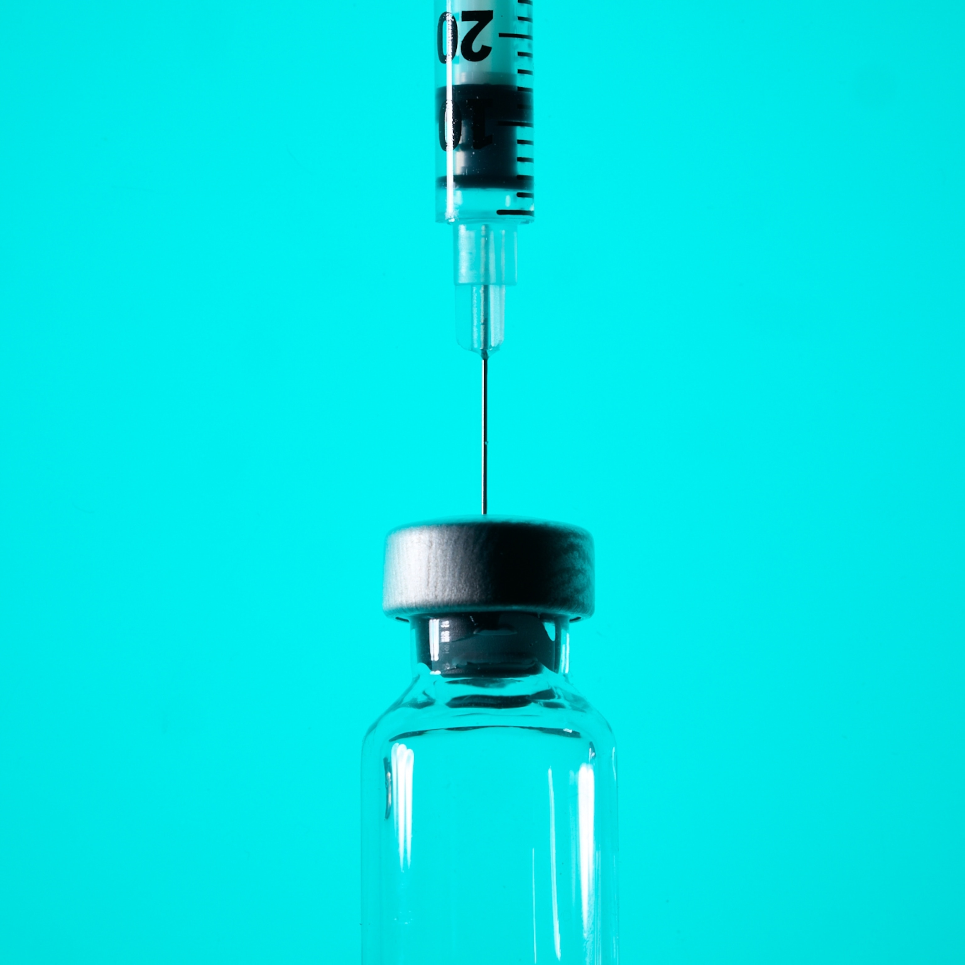 A close-up view of a needle and syringe and a glass vial, mostly in silhouette against a teal background