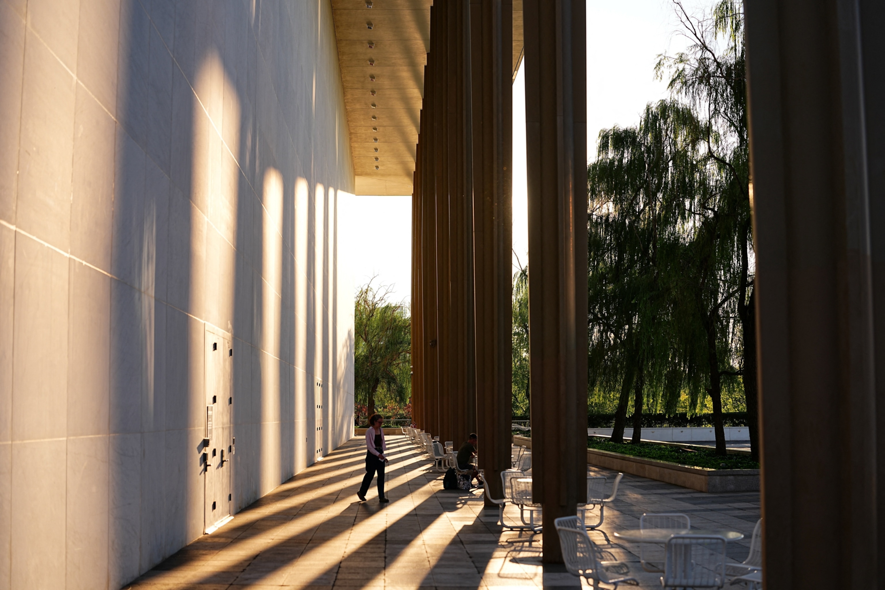 A woman walks across an entry way along tall columns.