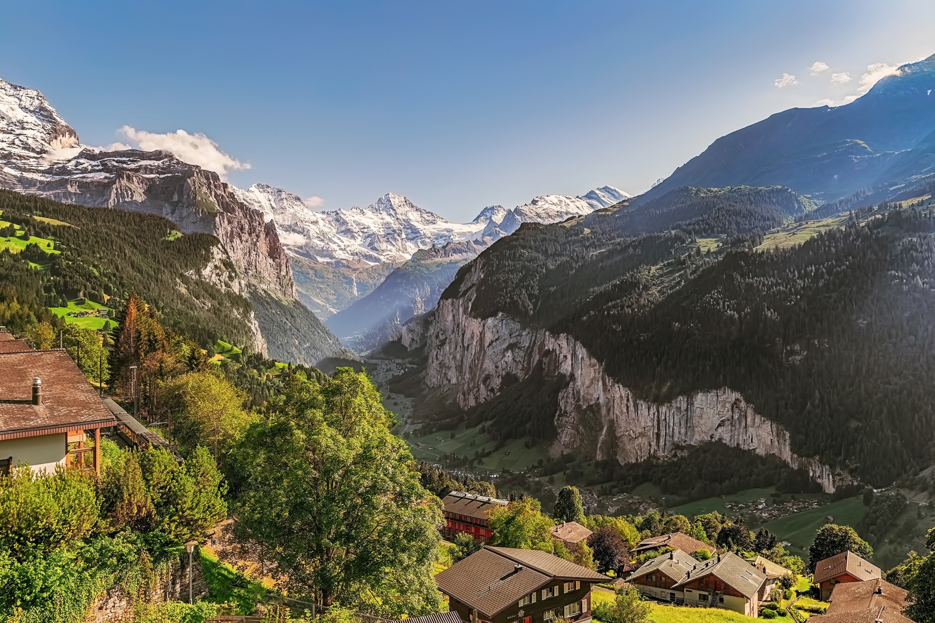 A scenic mountain valley shot with snow-capped mountains in the background and a small village nestled in between.