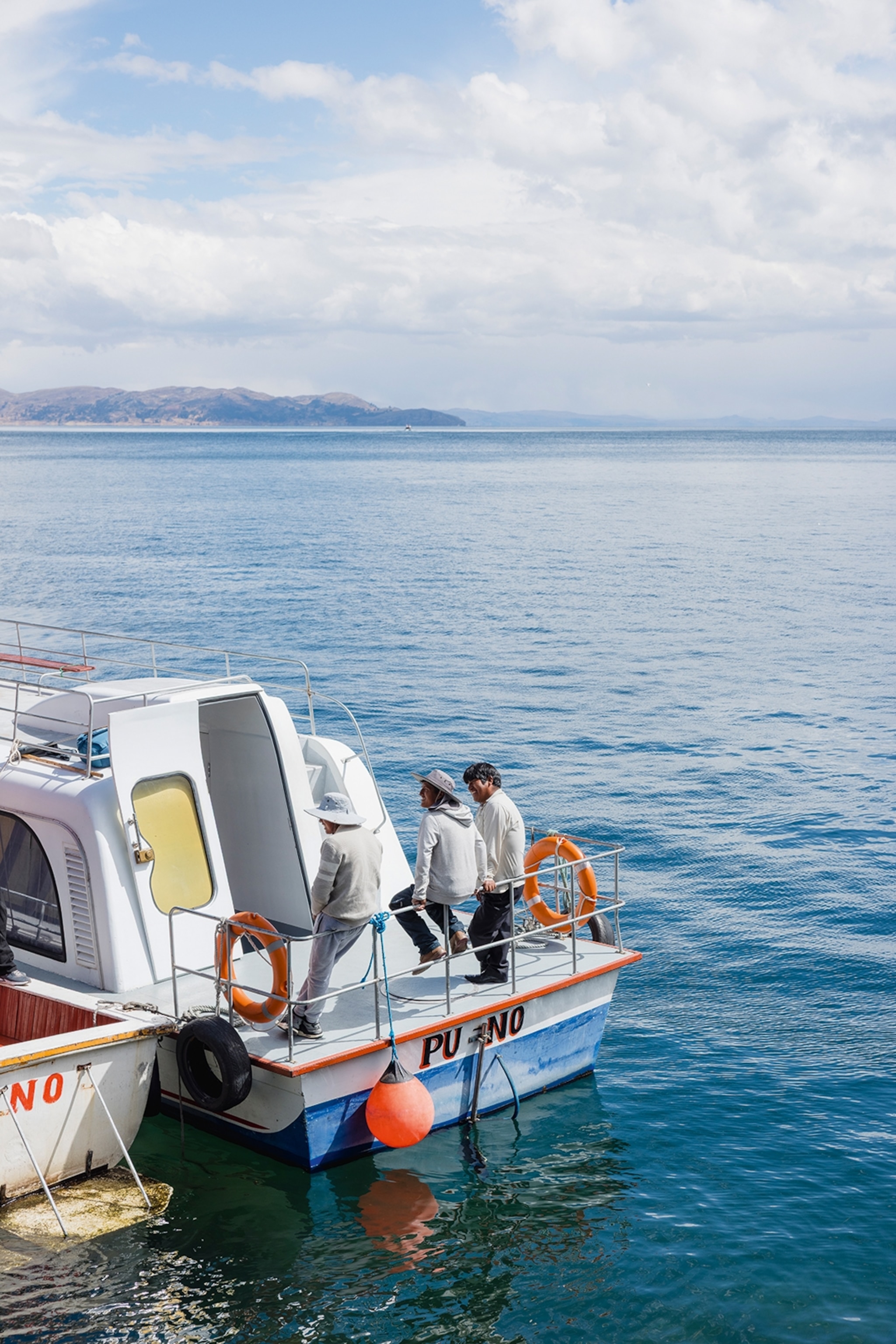 Three men casually leaning against the railing of a small boat with their backs to the camera and the open lake spreading out in front.