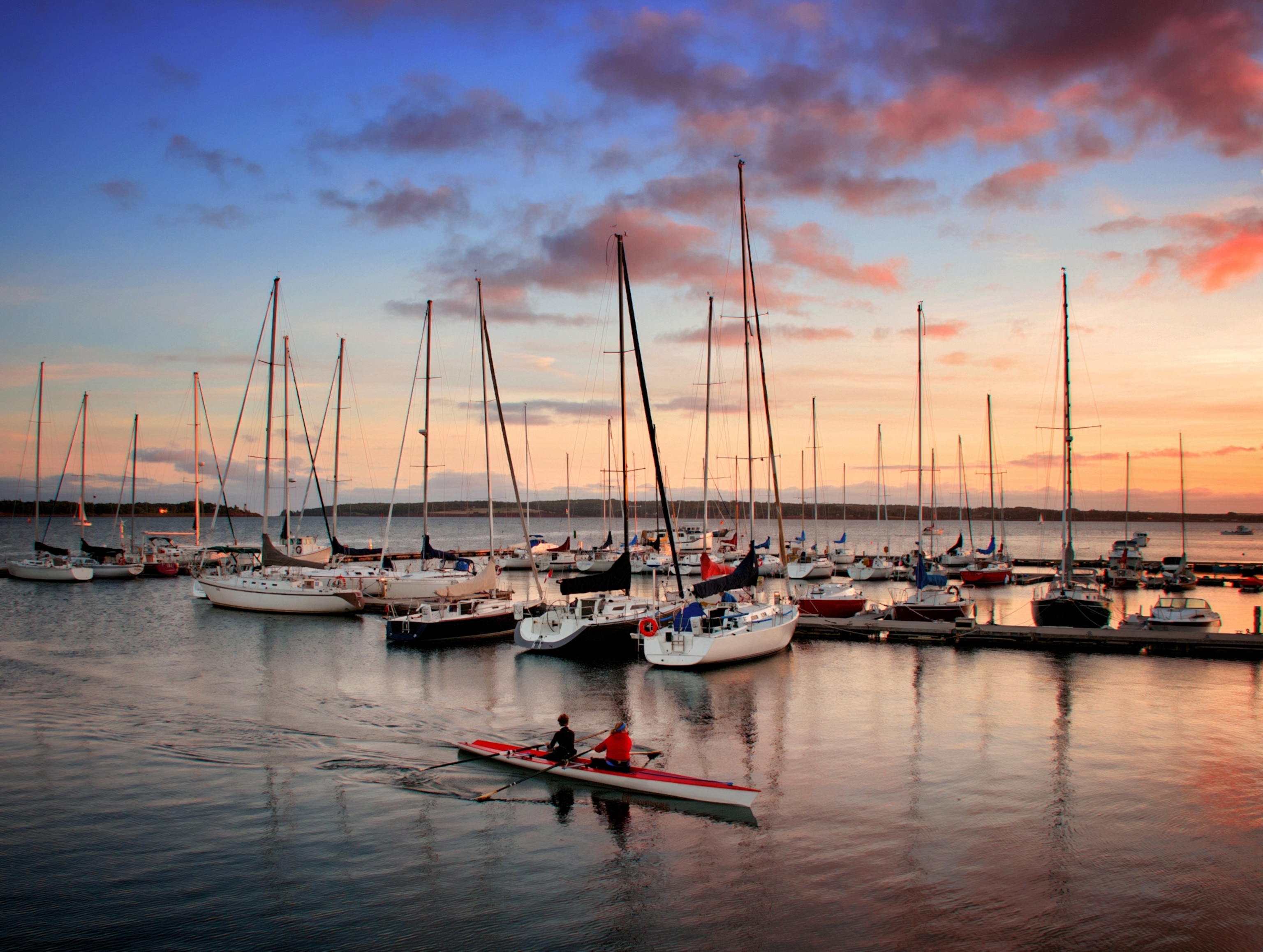 Kayakers coming into the harbour at Charlottown, Prince Edward Island, Canada at sunset with boats in the background and pink clouds forming.