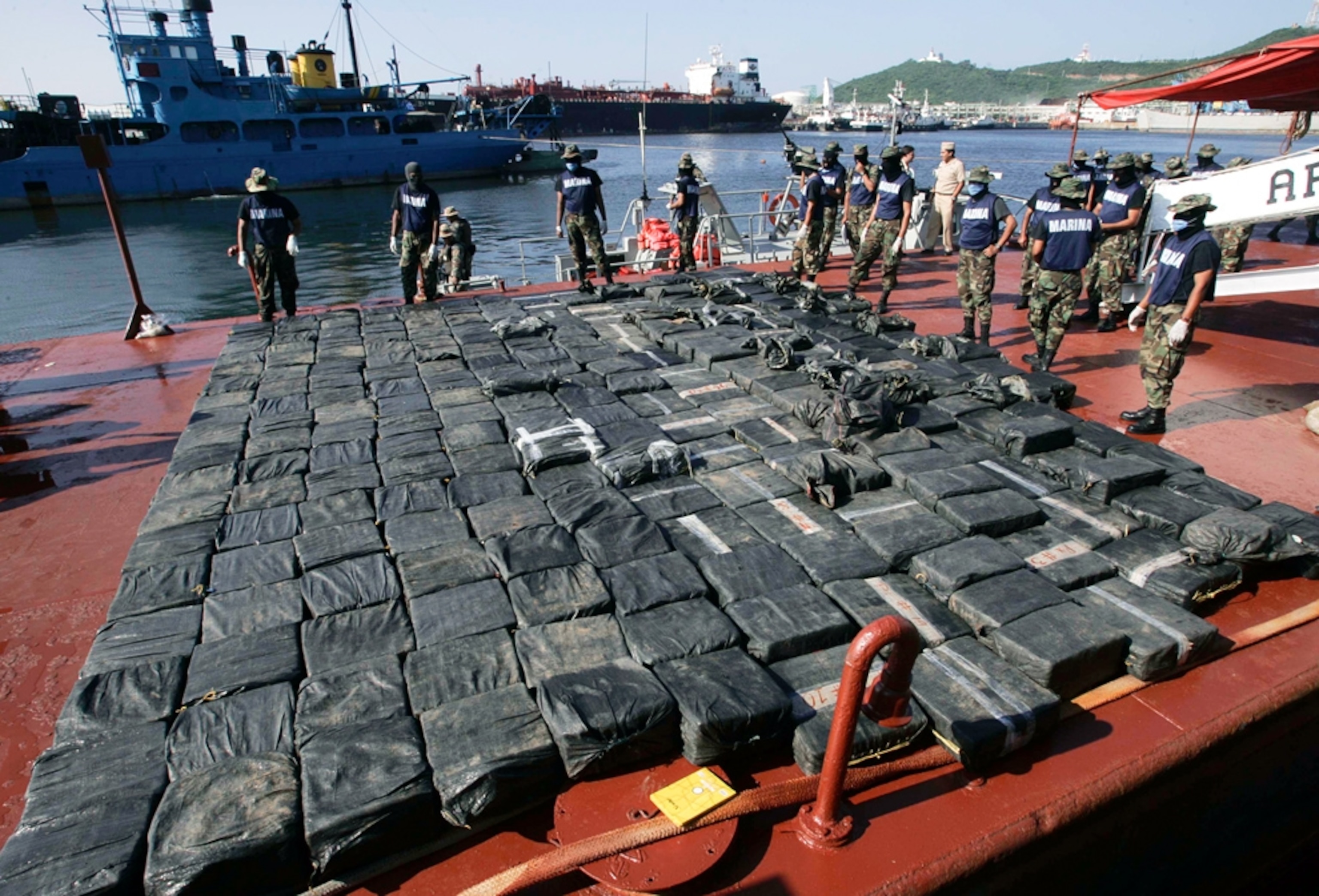 soldiers guarding a large pile of black packages, containing cocaine, arrayed on a dock