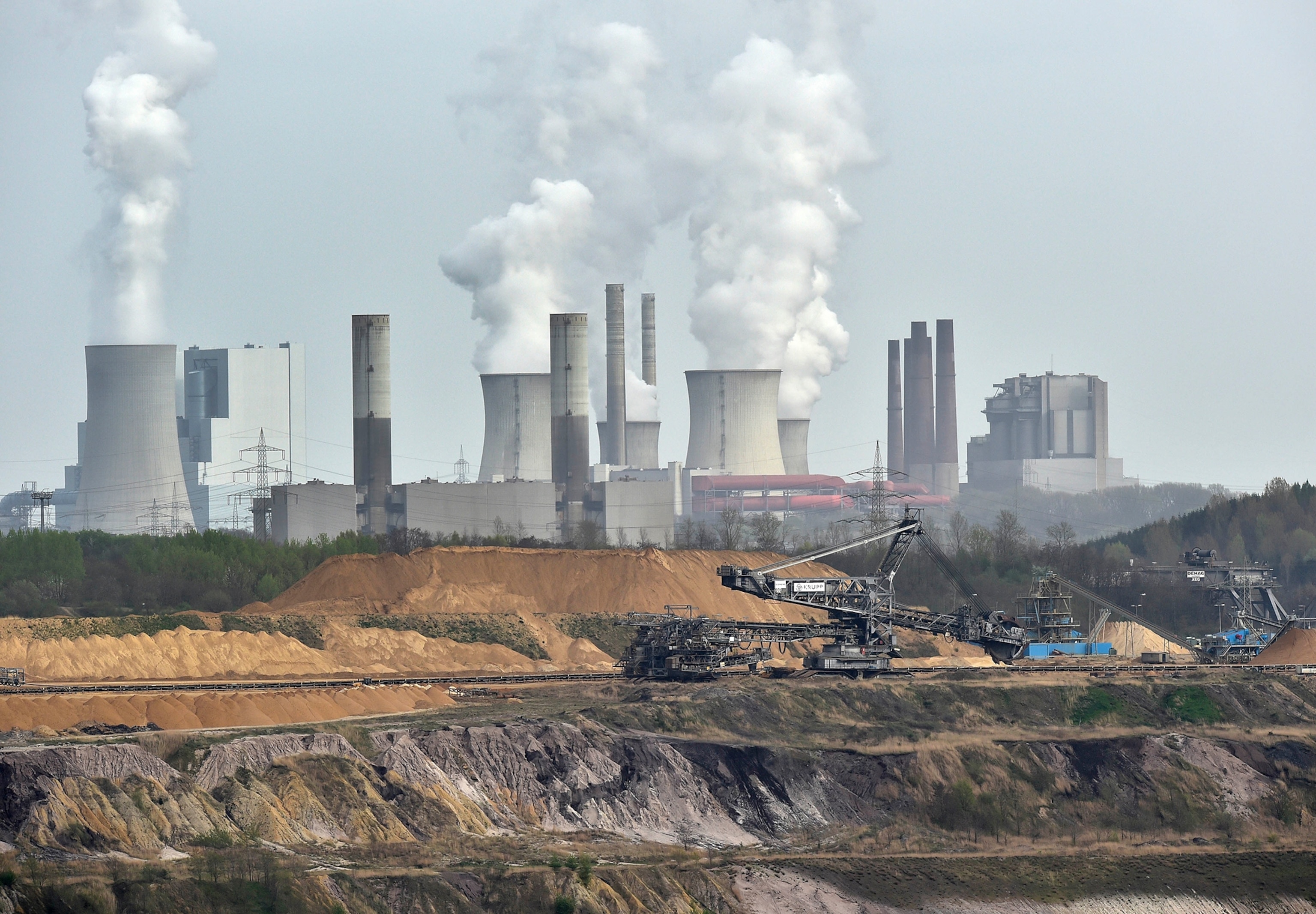 In this picture taken Thursday, April 3, 2014, giant machines dig for brown coal at the open-cast mining Garzweiler in front of a smoking power plant near the city of Grevenbroich in western Germany.