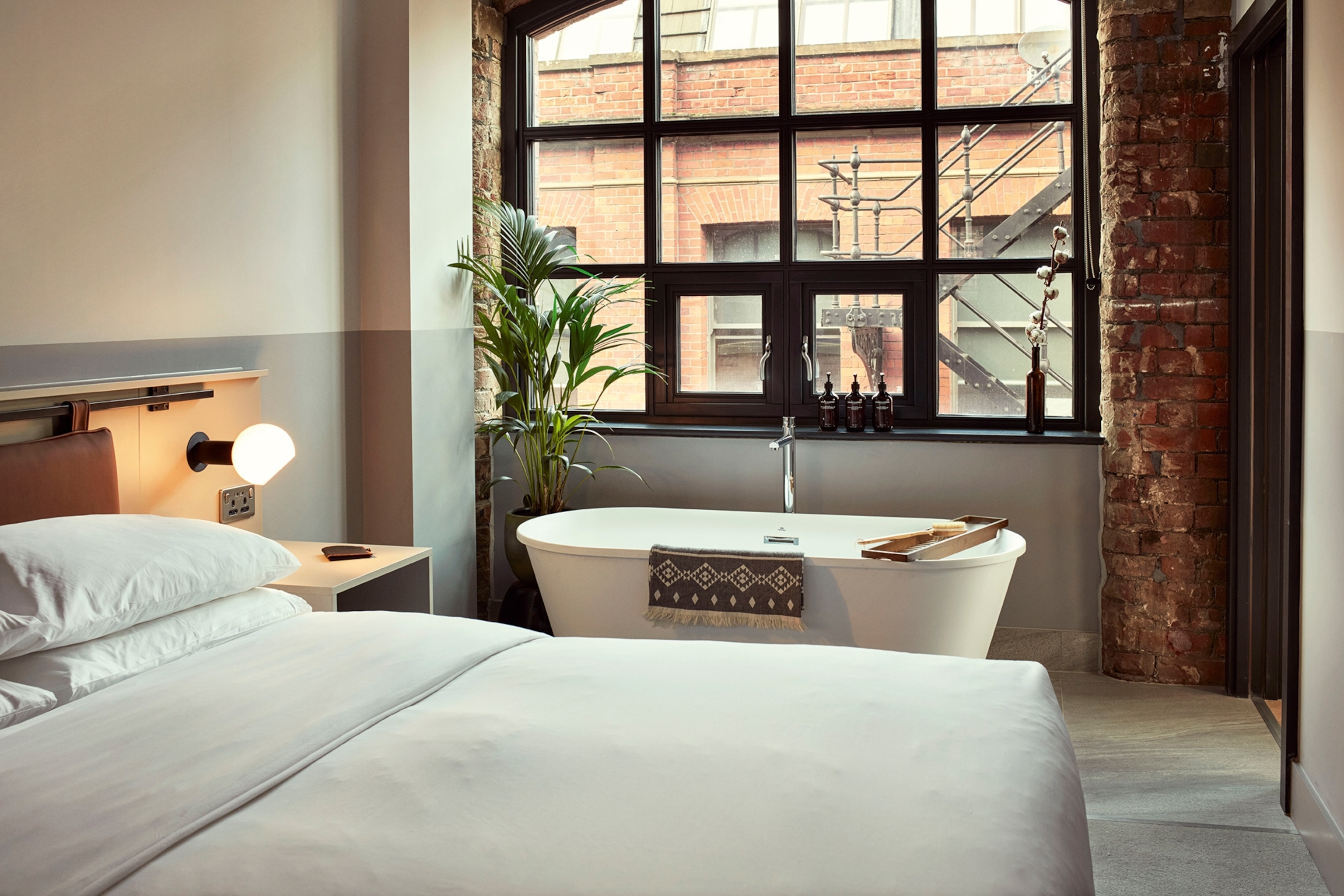 An industrial-style hotel bedroom with a free standing bath tub.