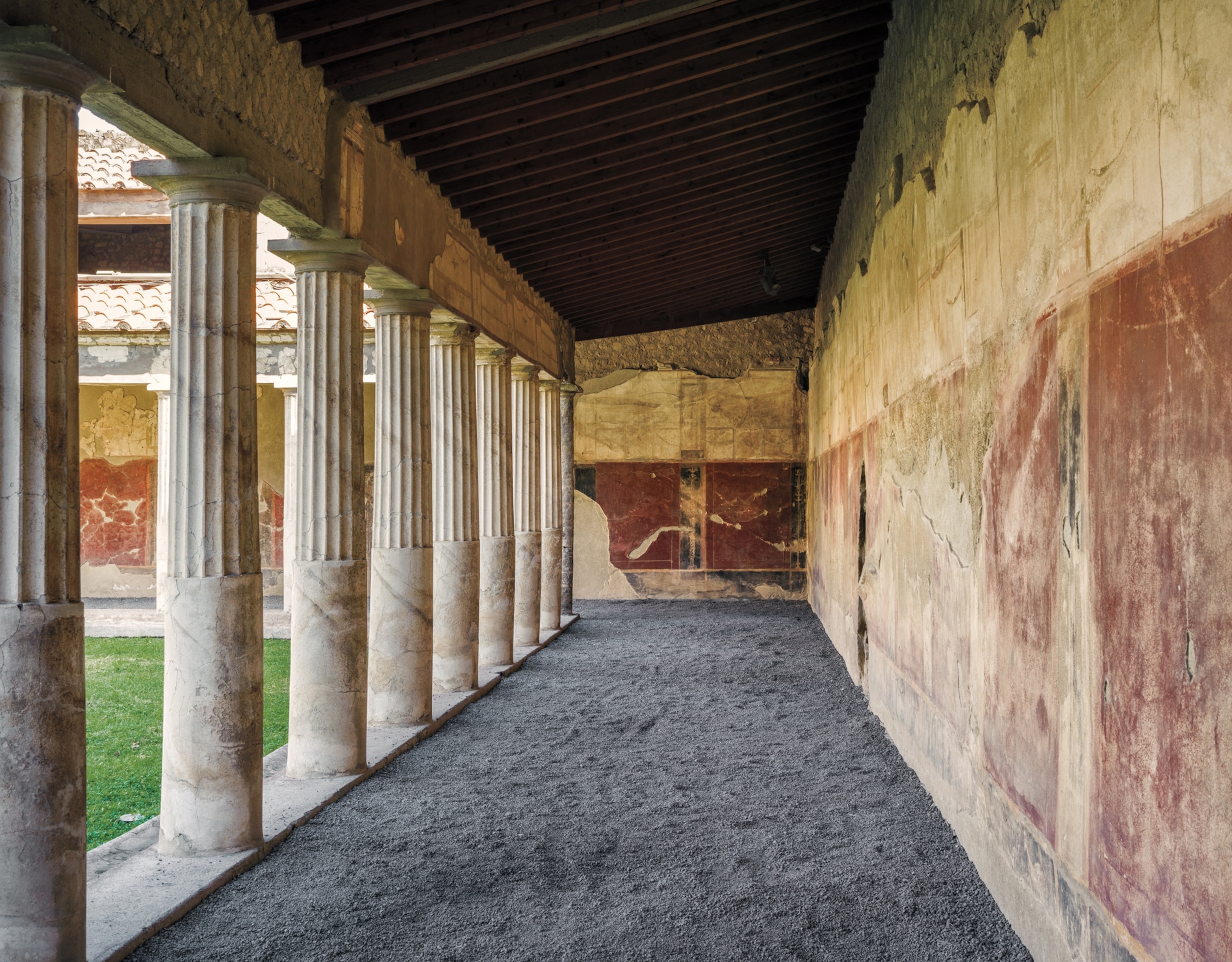 A stretch of walkway between a wall with old frescoes and columns.
