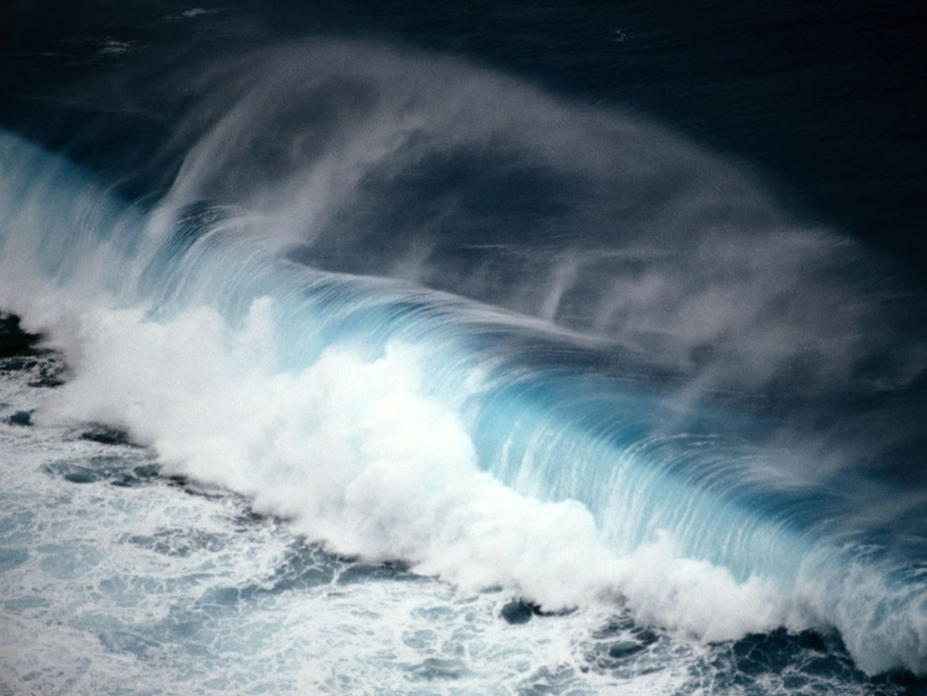 This aerial view captures a large wave crashing into the coastline of an island in the Republic of Palau