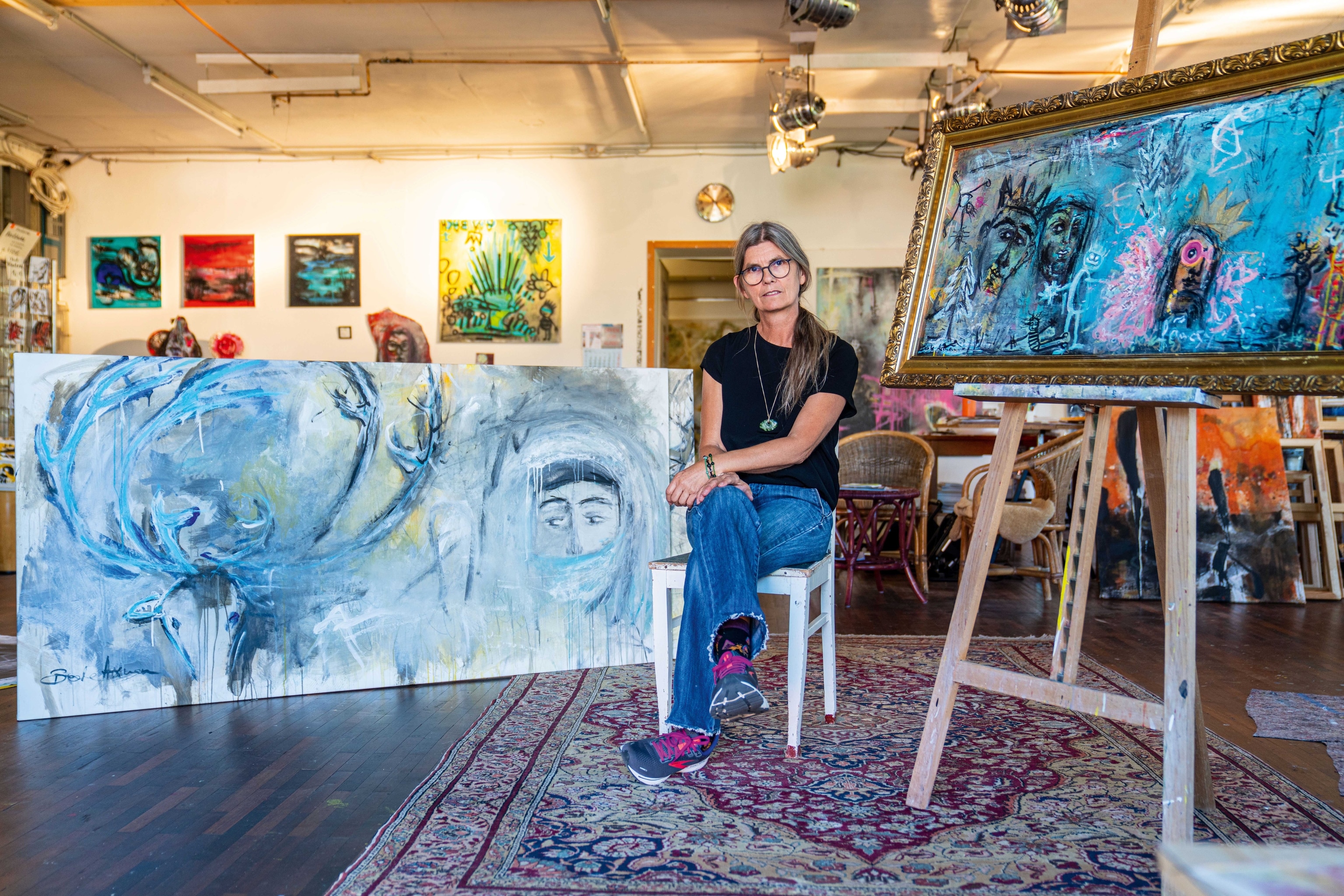 An artist sits in front of a selection of paintings.