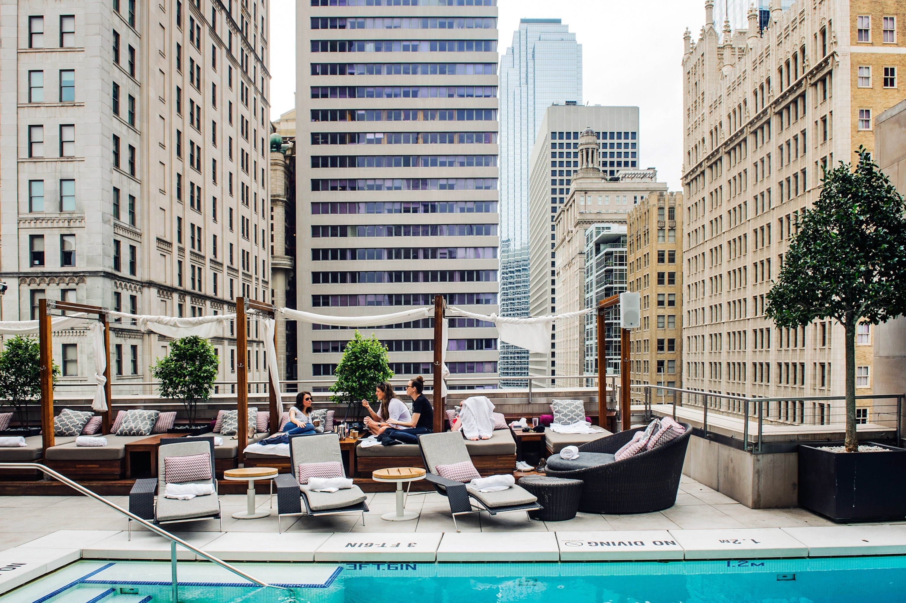 People lounge in front of a pool with a skyline behind them.