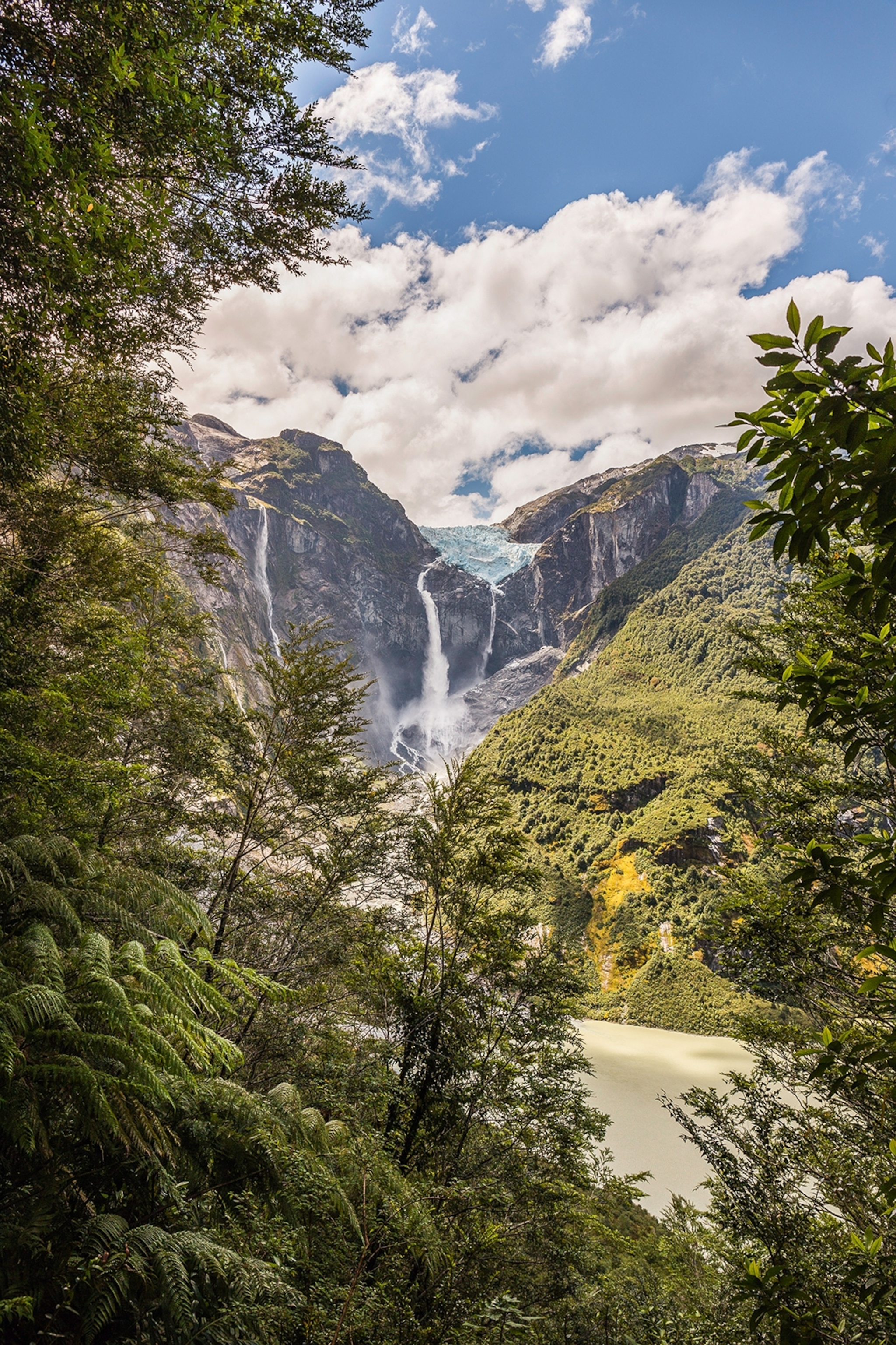 A lush mountain scene from a hiking perspective with a waterfall in the distance.
