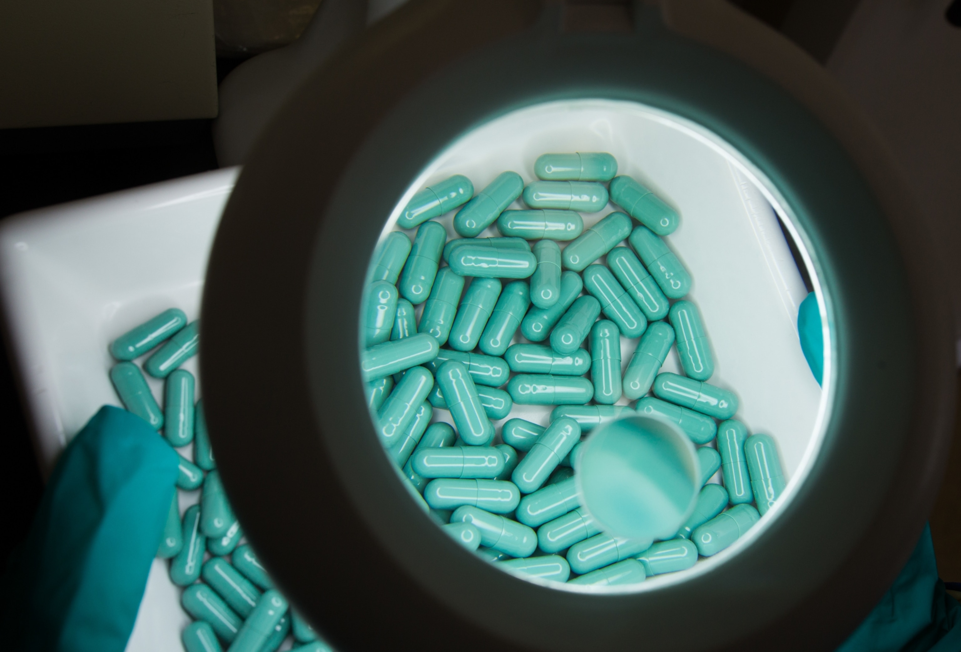 Blue pill capsules being observed under a large magnifying glass.