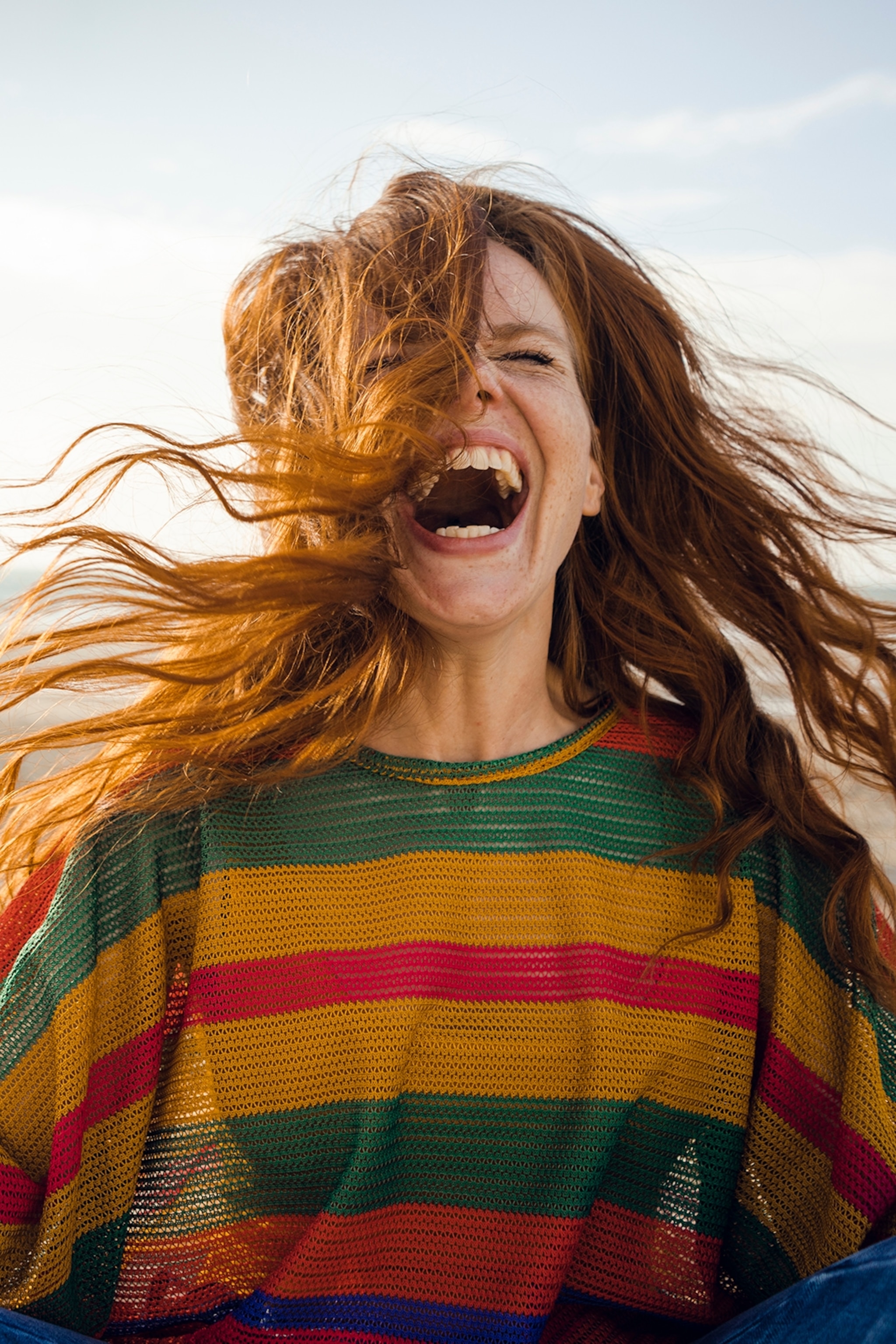 A woman with long hair screaming enthusiastically into the camera with her eyes closed.