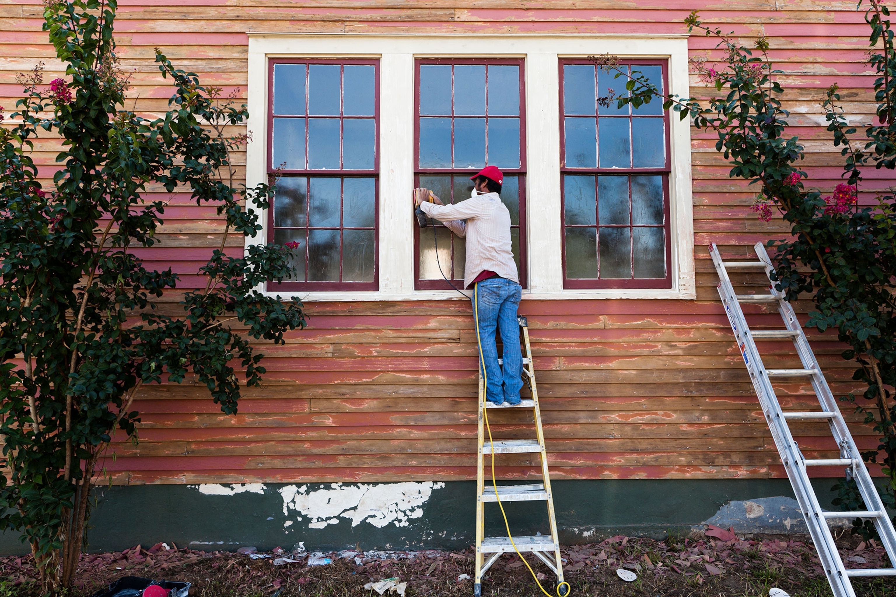 a man sanding lead-based paint off of a house
