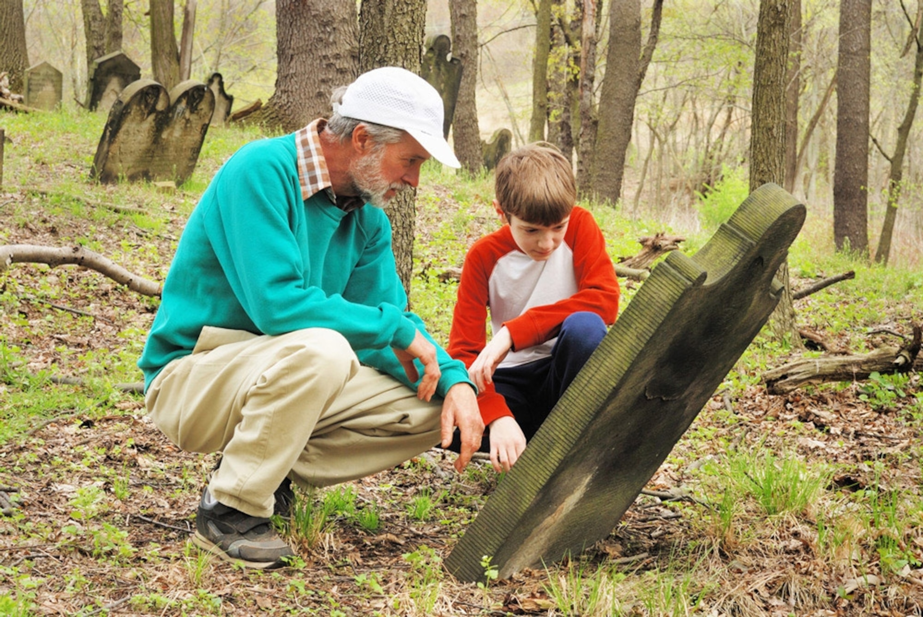 Man and boy view gravestone in old cemetery. Researching ancestors, history. Grandfather / grandson relationship. Family tree.
