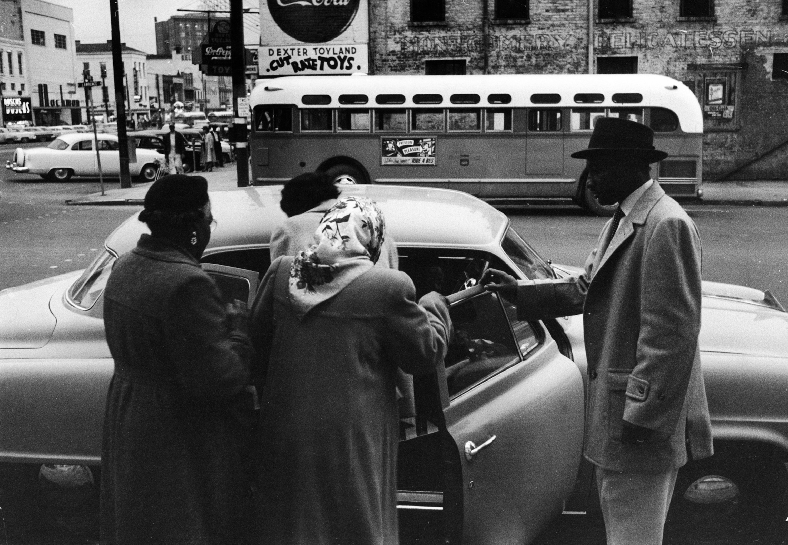 A group of African Americans getting into a car as an empty city bus drives past