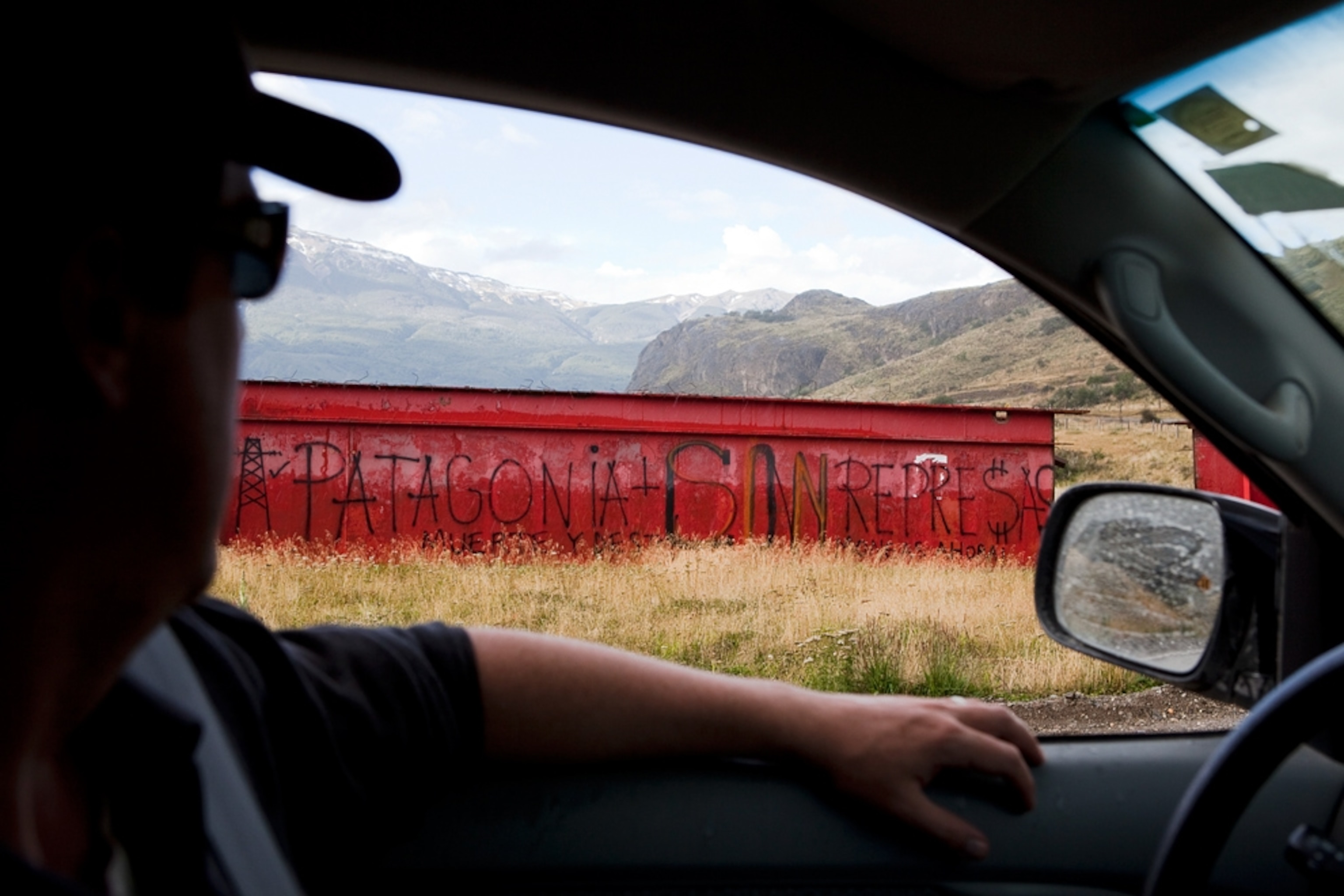 A man looks through a car window at graffiti decrying a proposed hydroelectric project