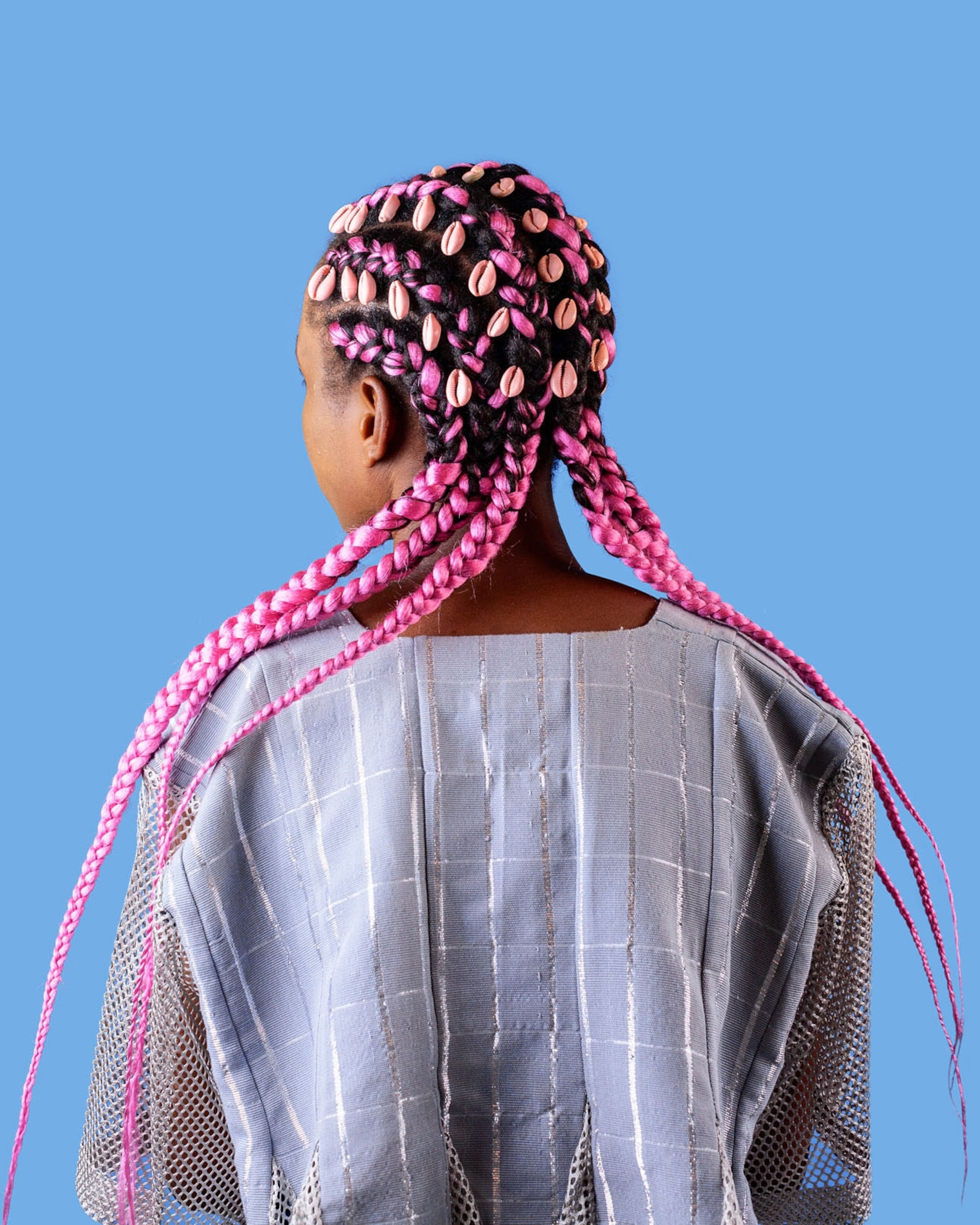 Picture of a woman with hair sectioned using pink extensions and braided along with the woman’s hair. Medina spray-painted the shells pink before they were sewn in.