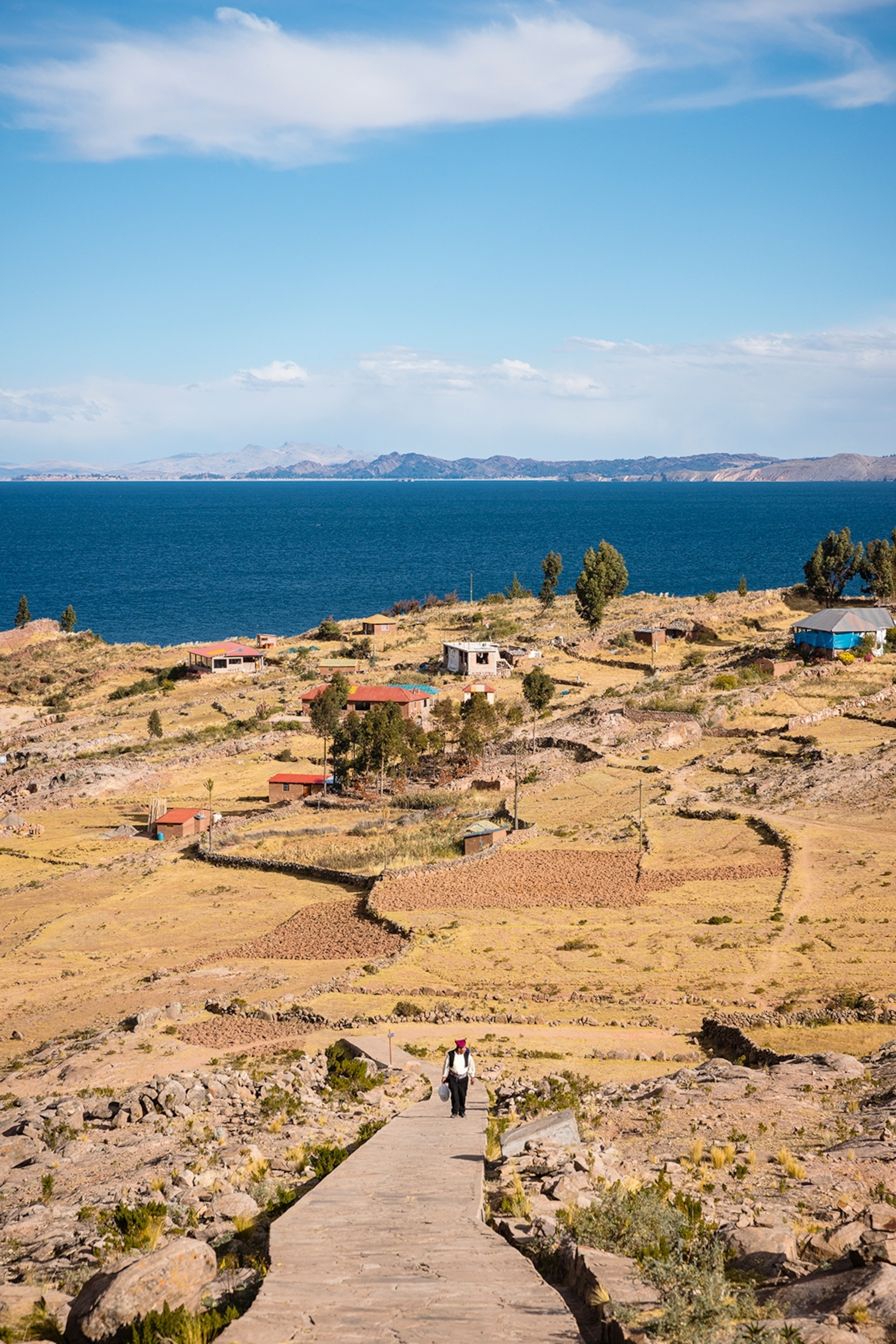 A man walking along a path with a flat and mostly arid landscape stretching out behind him.