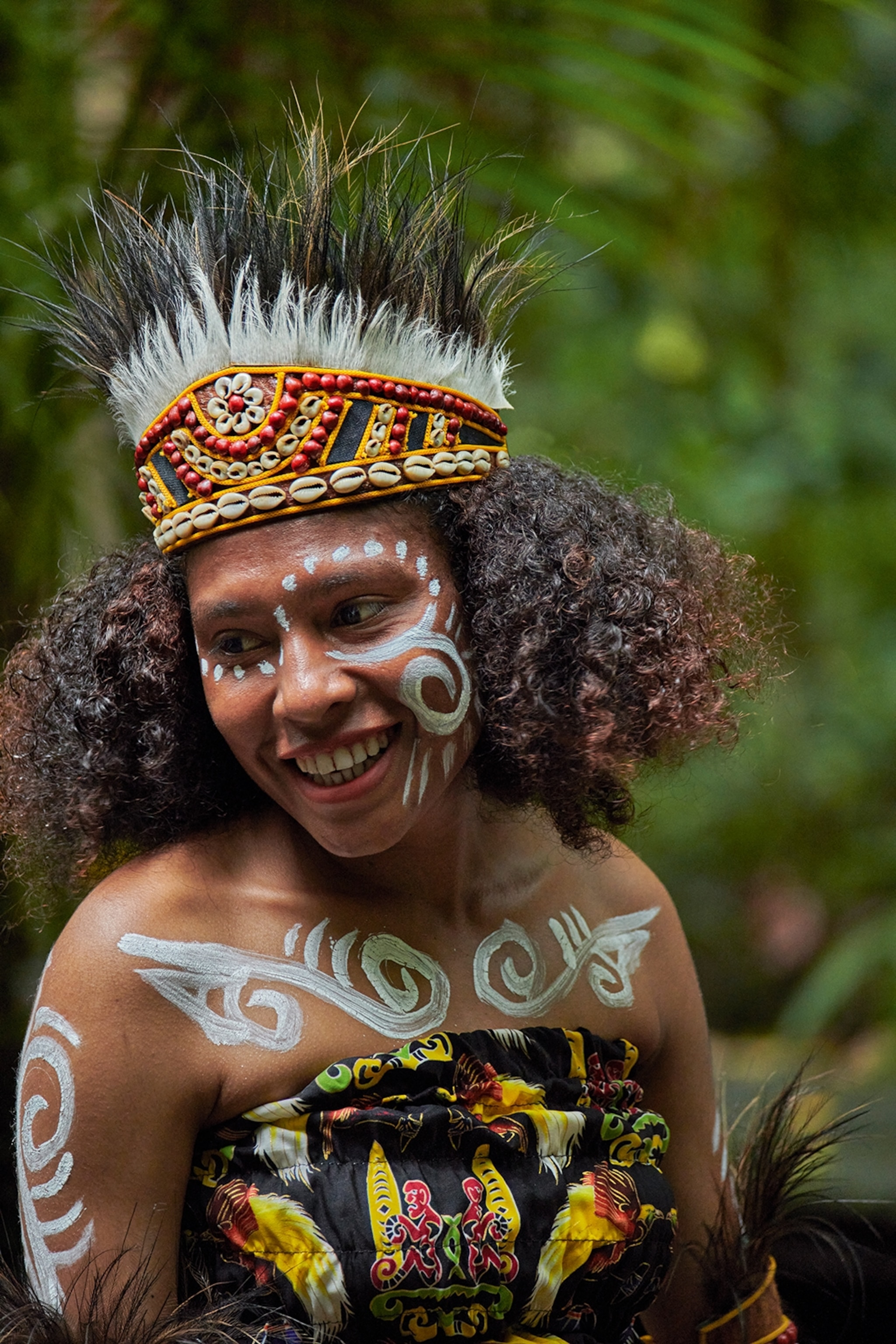 A portrait of a smiling local woman wearing traditional dress complete with body painting and a head dress with feathers.
