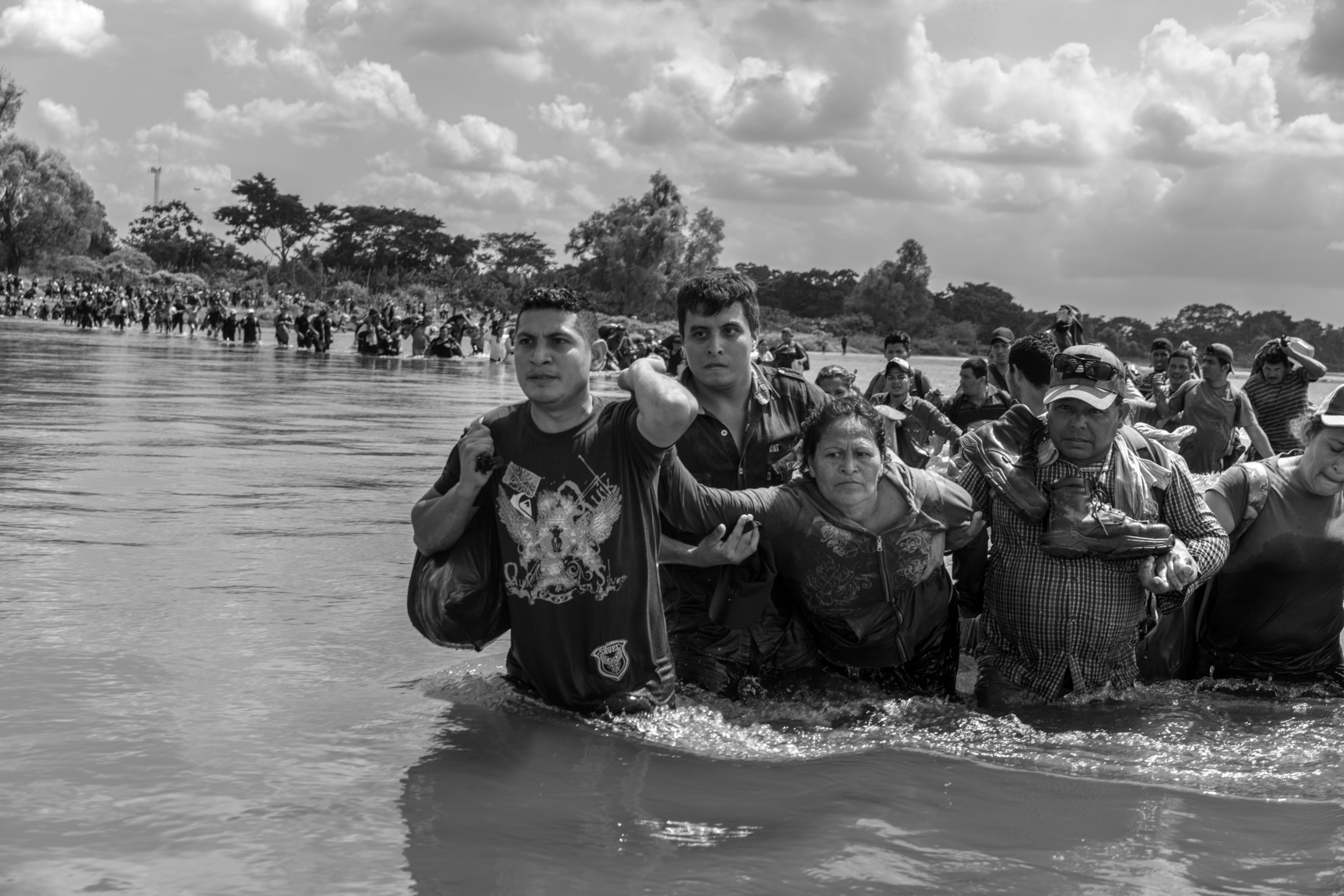 people walking across a river as a group of men support a woman
