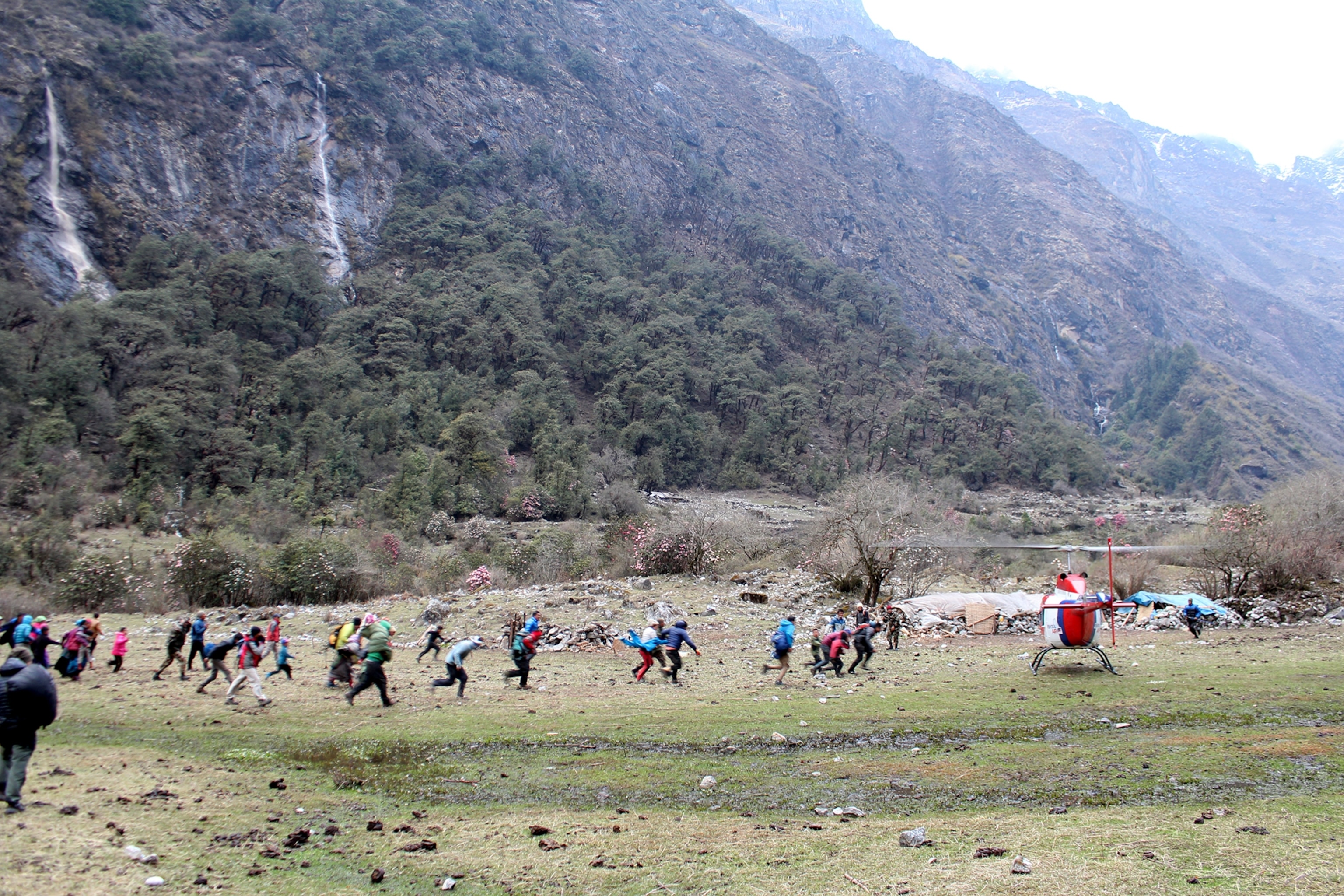 Survivors assembled in a field at Godhatabela run for a private helicopter as it lands