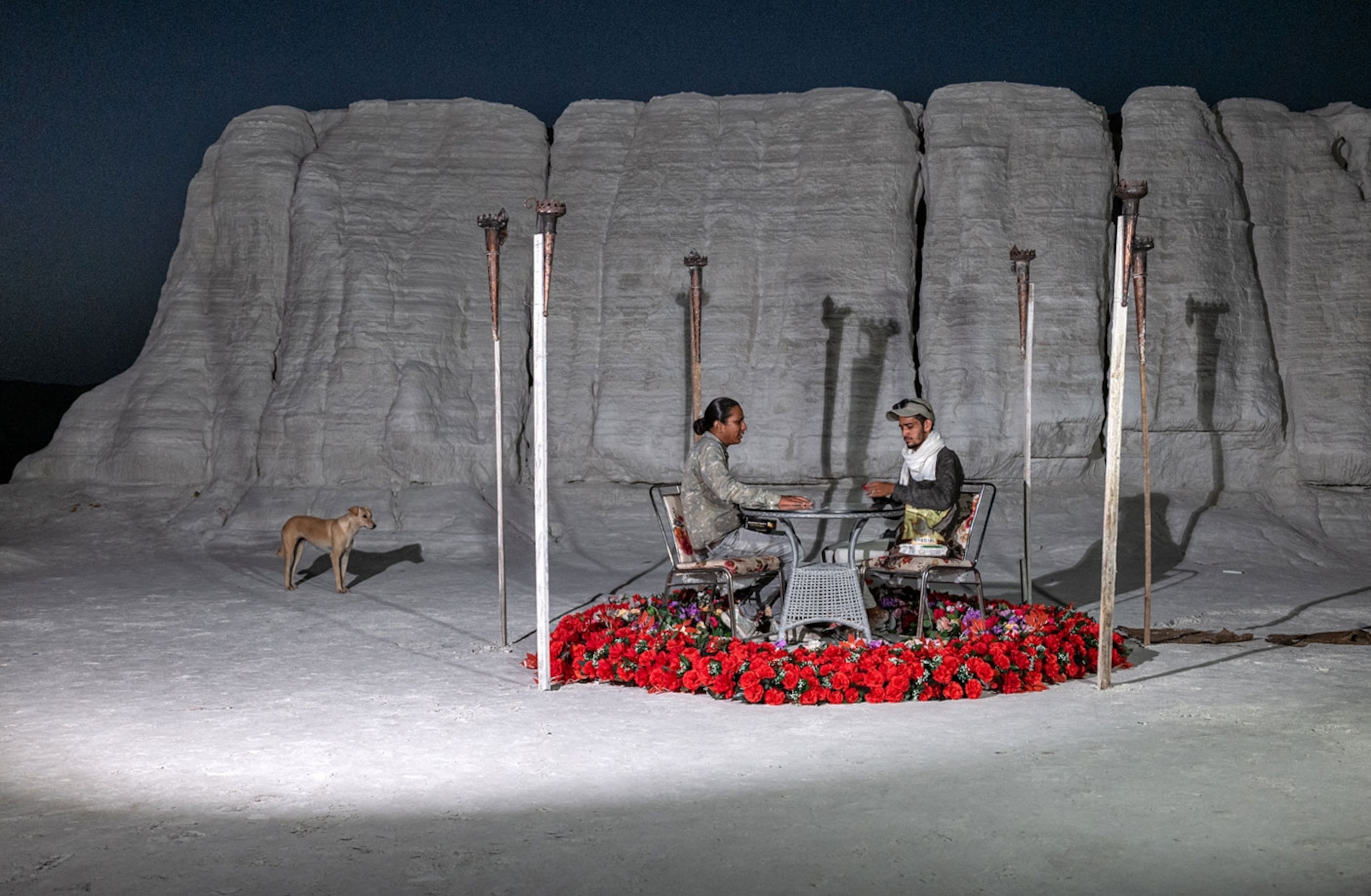 A man two men sit at table with a dog in the distance.