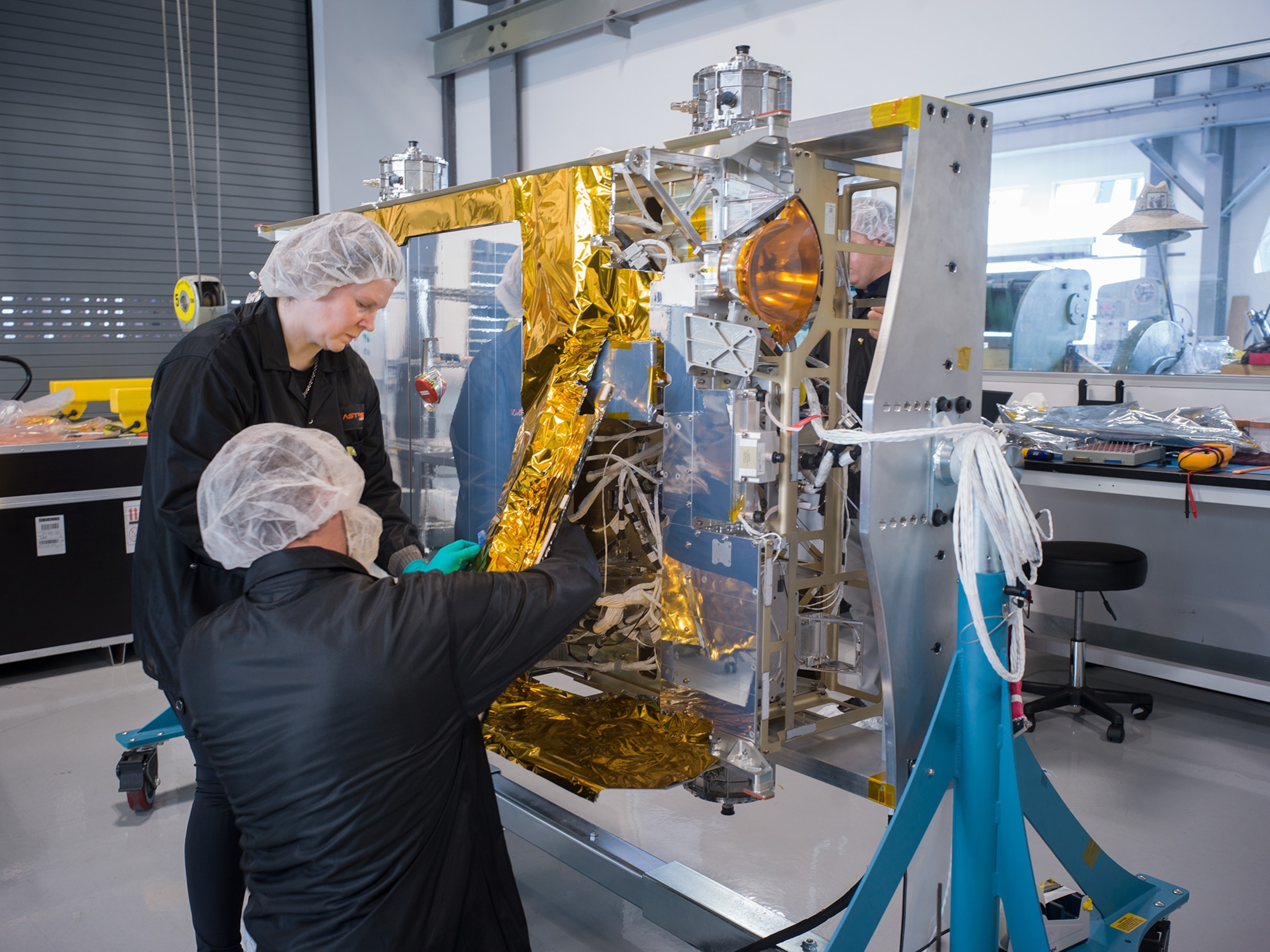 two people with hair nets on working in front of a panel of wires and steel