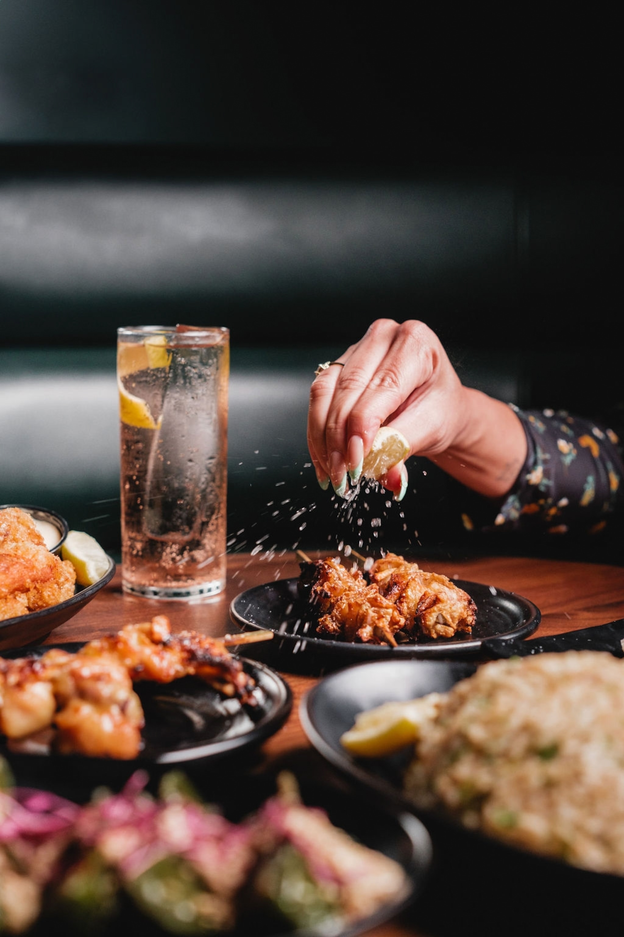 A woman's hand squeezing fresh lemon onto skewers of fried seafood