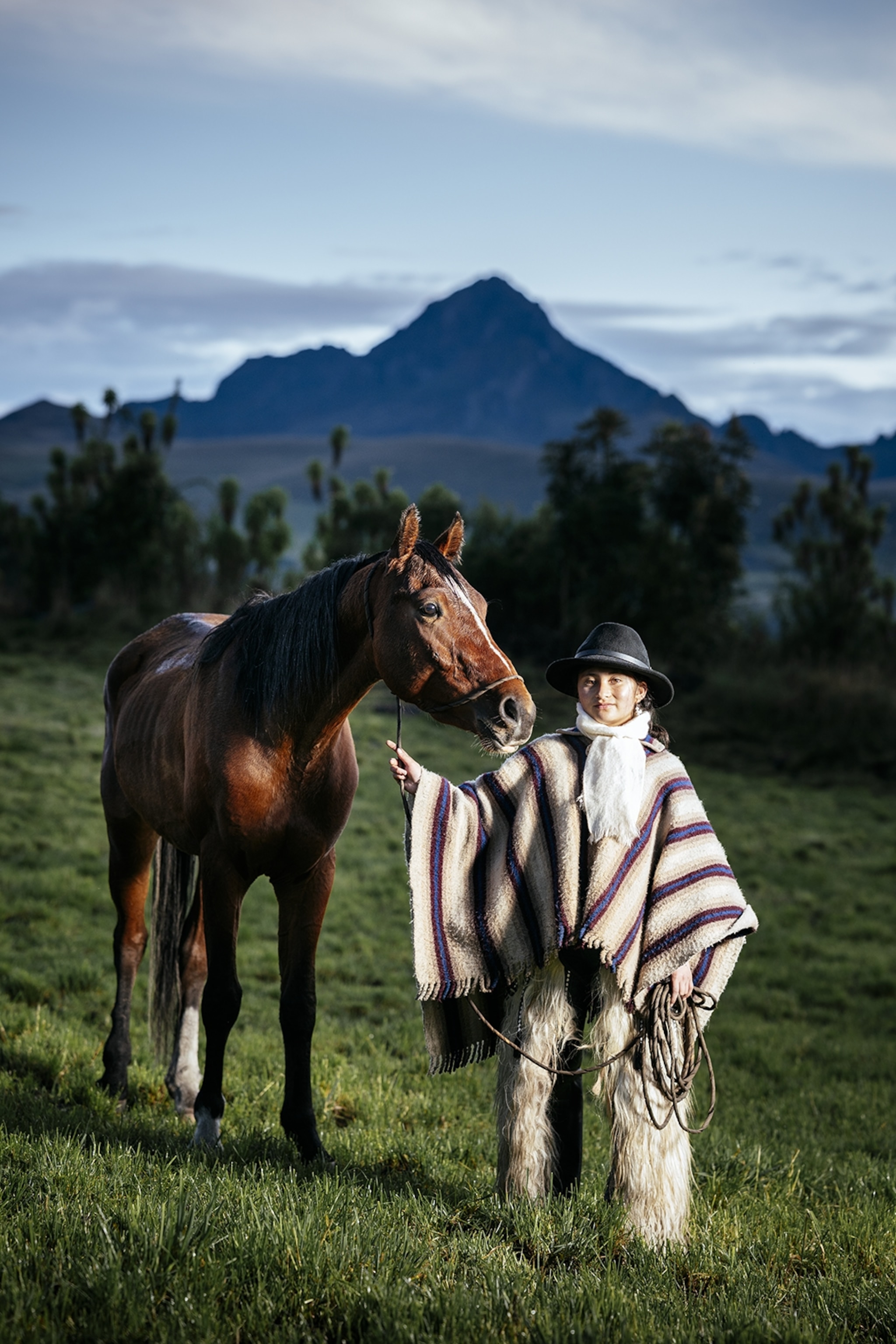 A young cowgirl in Ecuador standing next to a horse in the mountains.