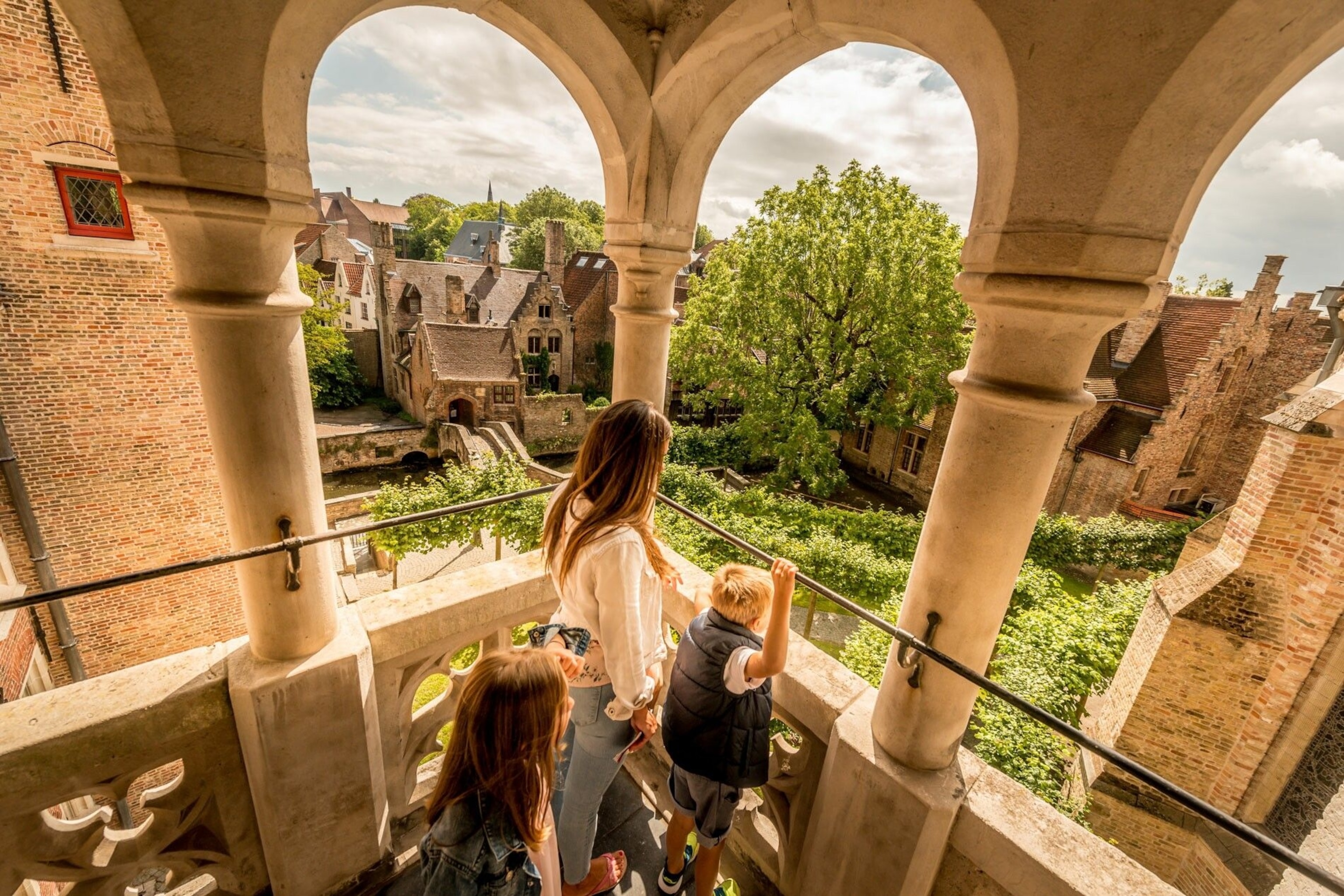 People looking from between the columns of a townhouse balcony at the shrubs and old bridges below