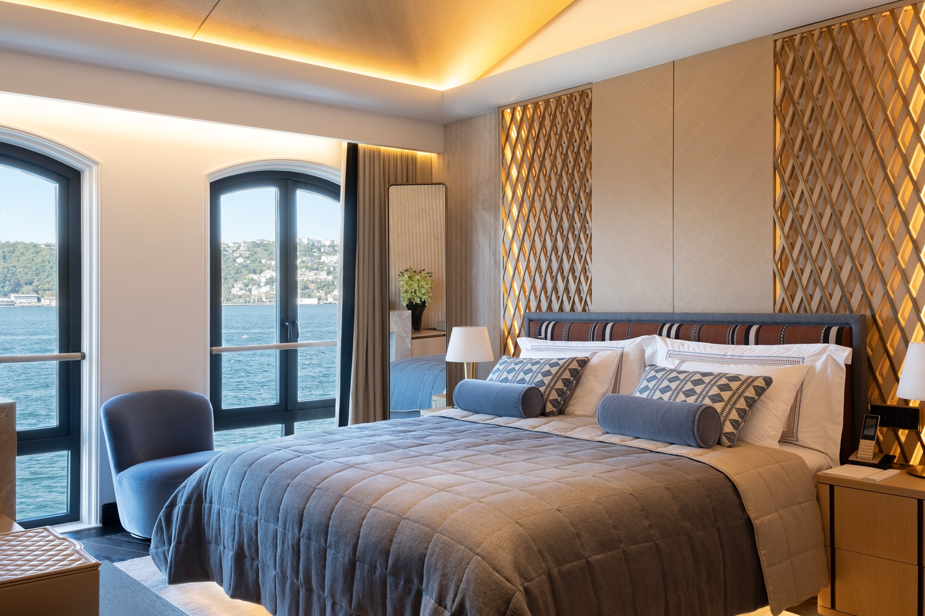 A queen-size, stylish hotel bedroom with two floor-length windows opening to the ocean.