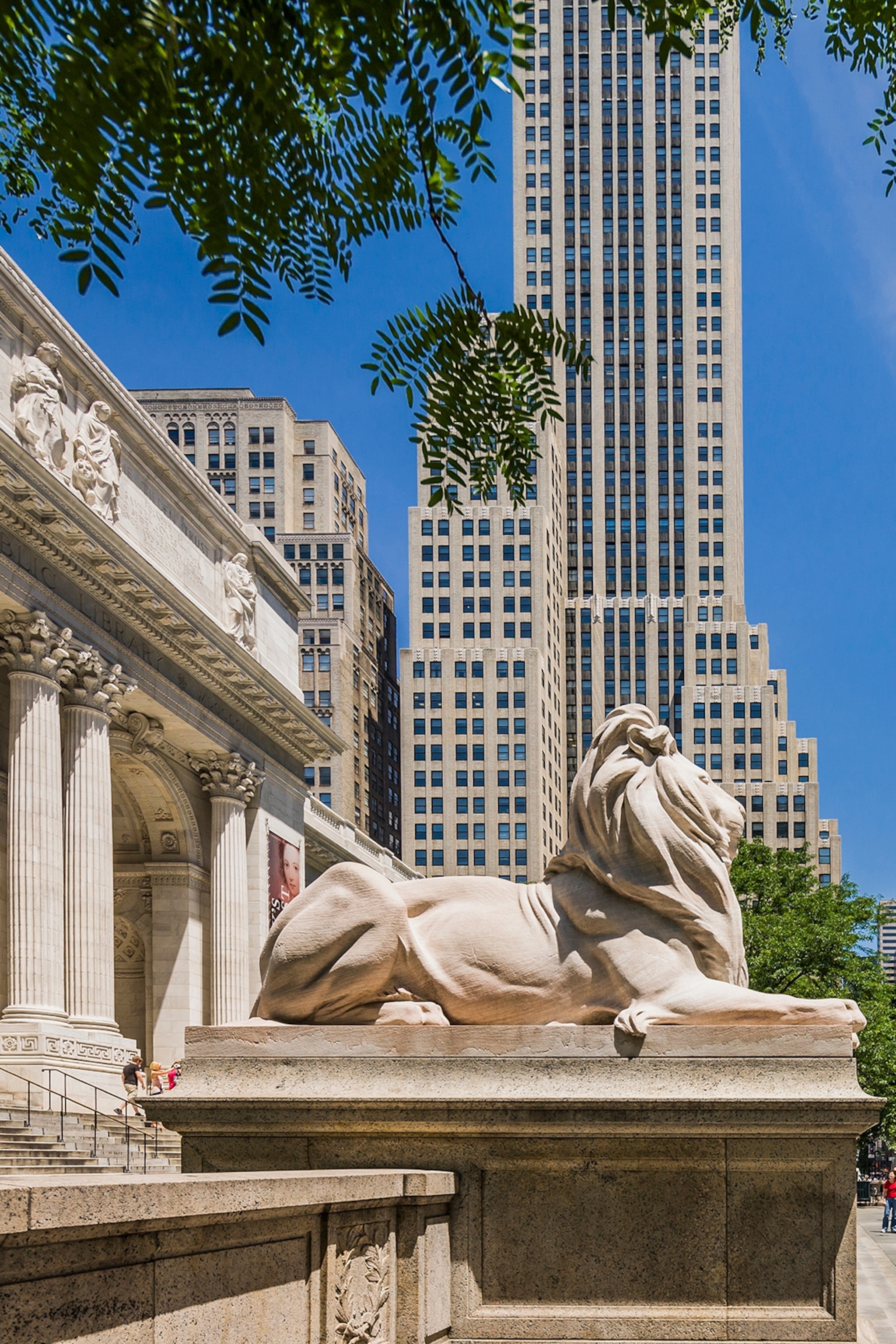 Stone lion outside a grand stone building with pillars, backed by a tall concrete skyscraper in the background