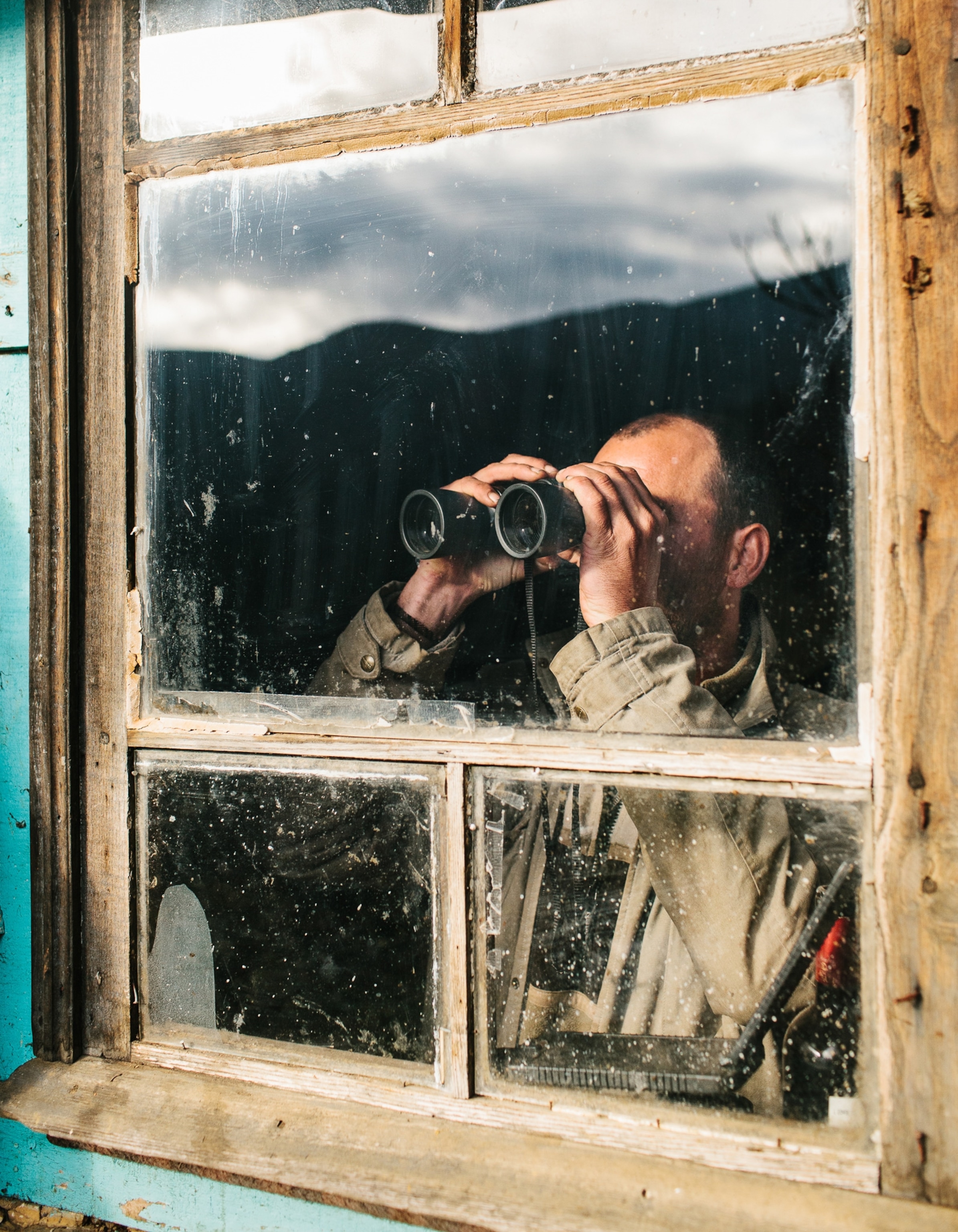 a man observing birds with binoculars through his window