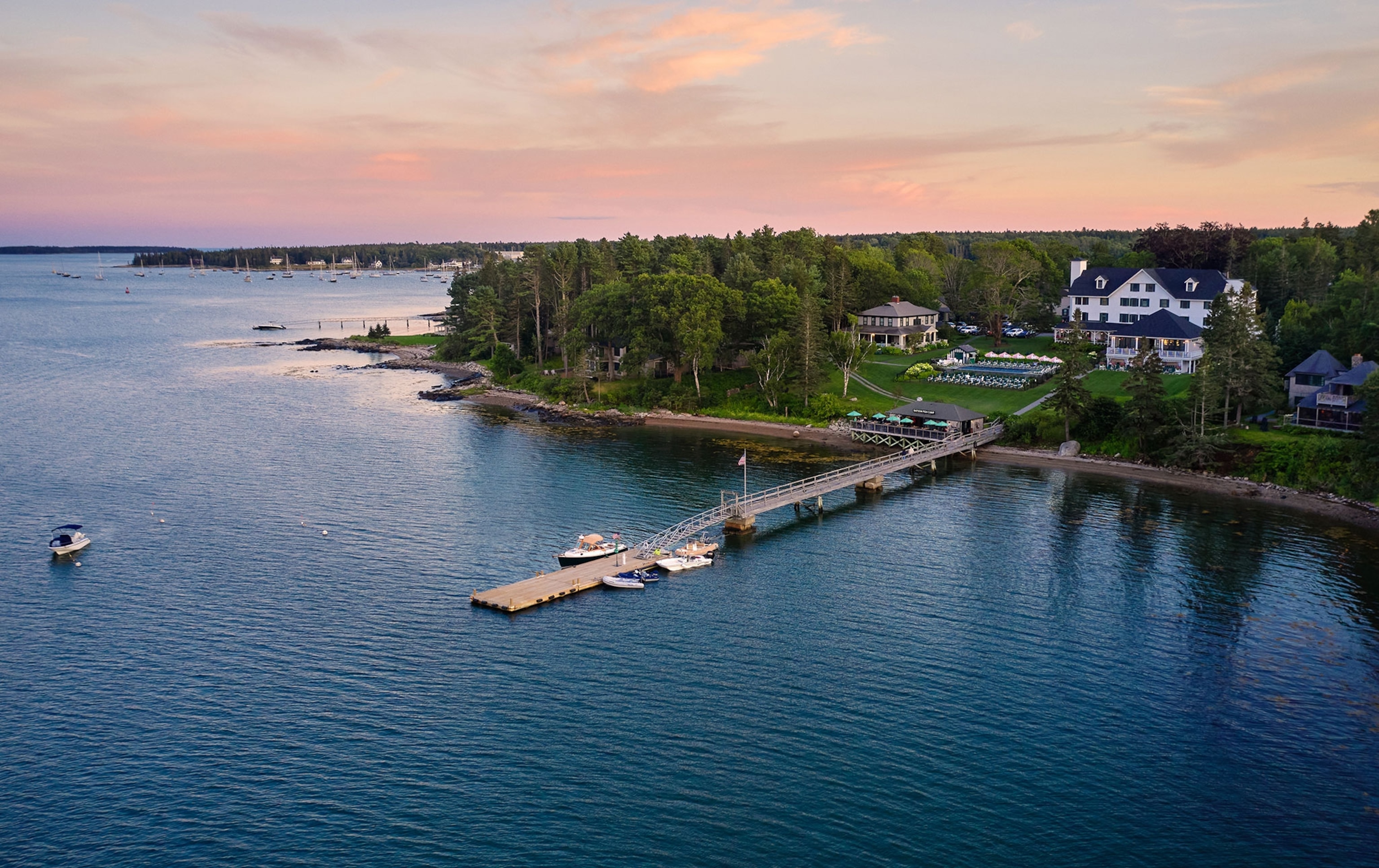 An aerial view of a lake with luxurious cabins and a white hotel on the shore with a dock extending into the lake.