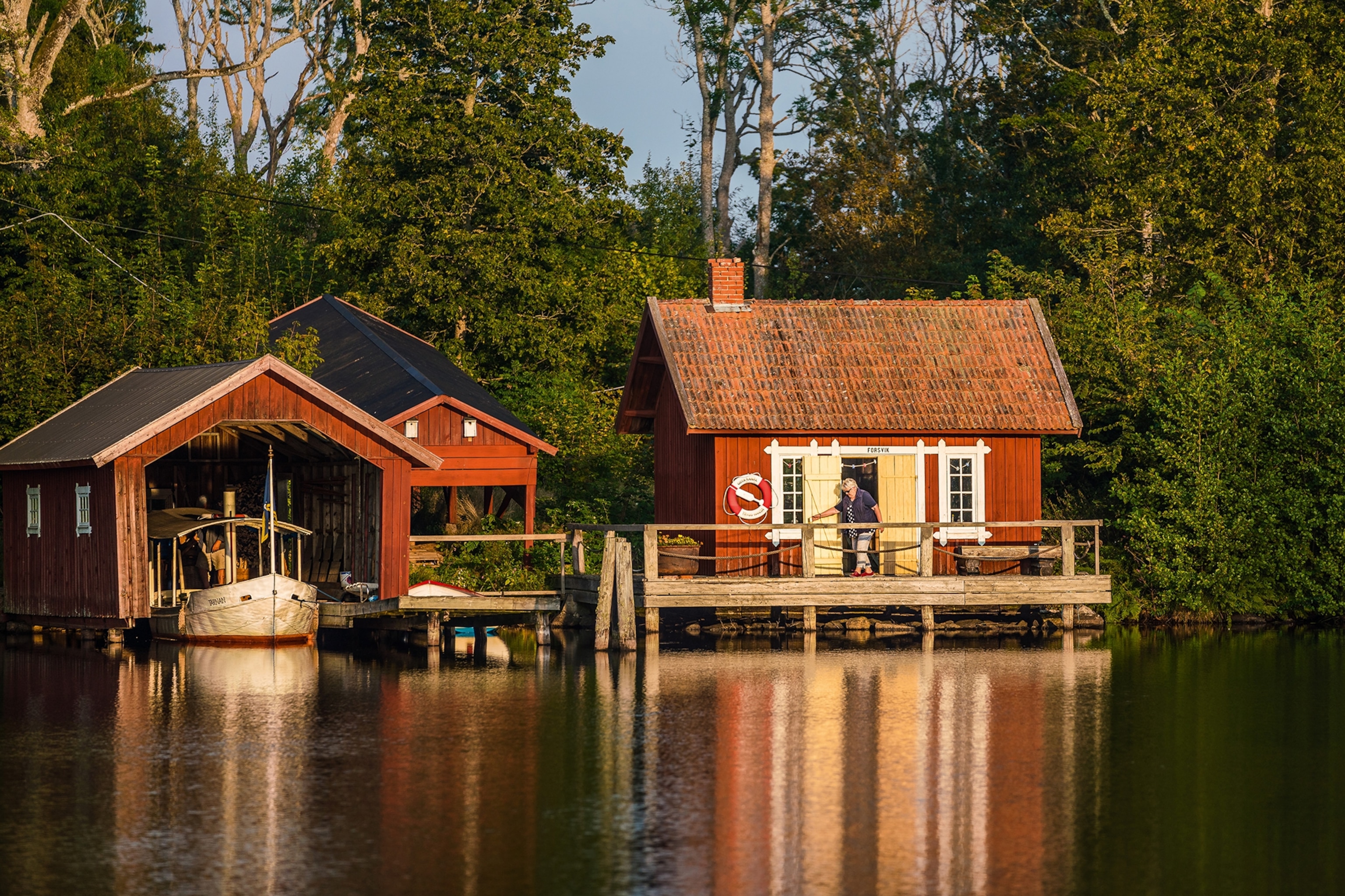A block house on a lake with trees in the back and a separate hut for an anchored boat.
