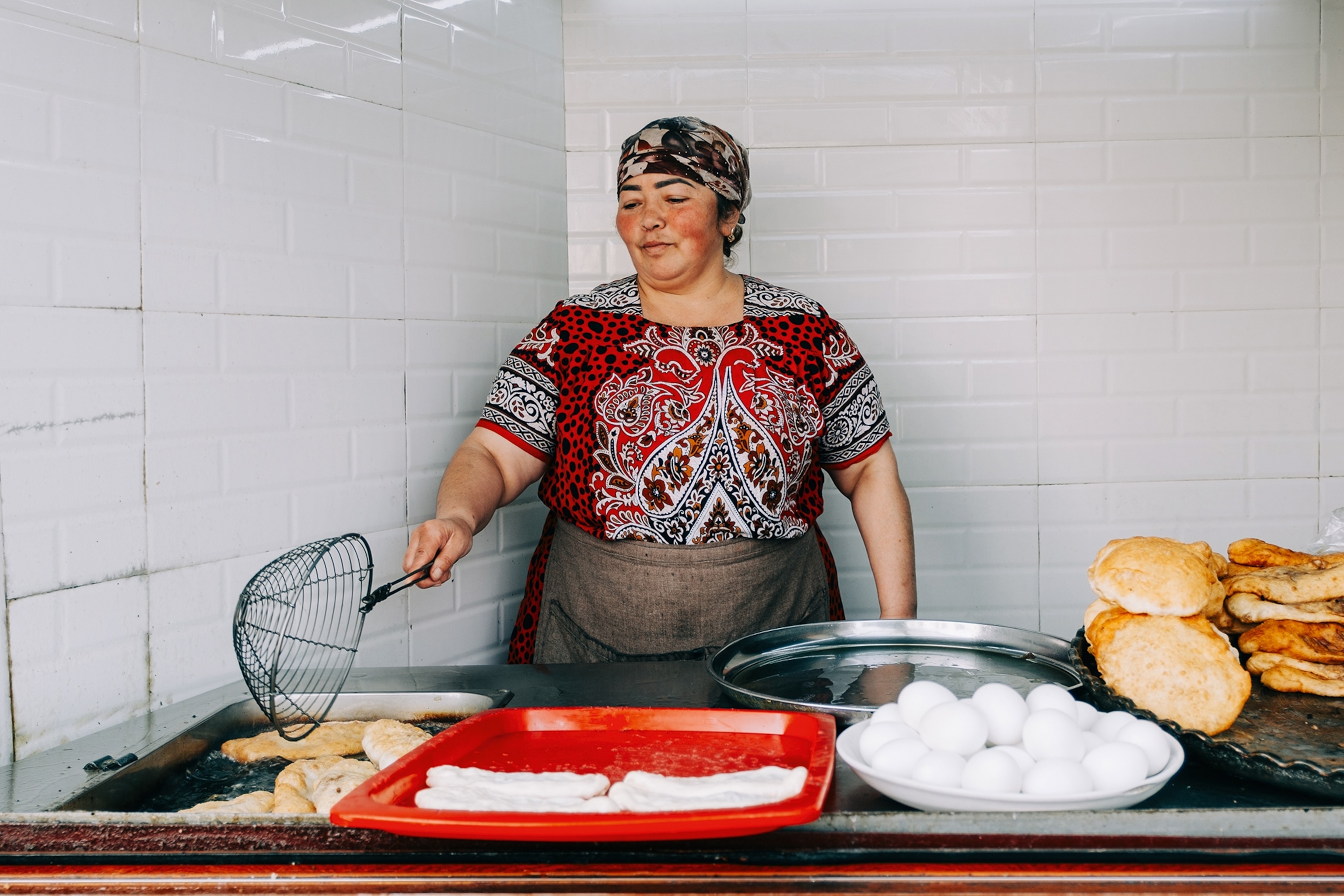 A local woman in a tiles kitchen corner fishing out puffed up bread from a frying station.