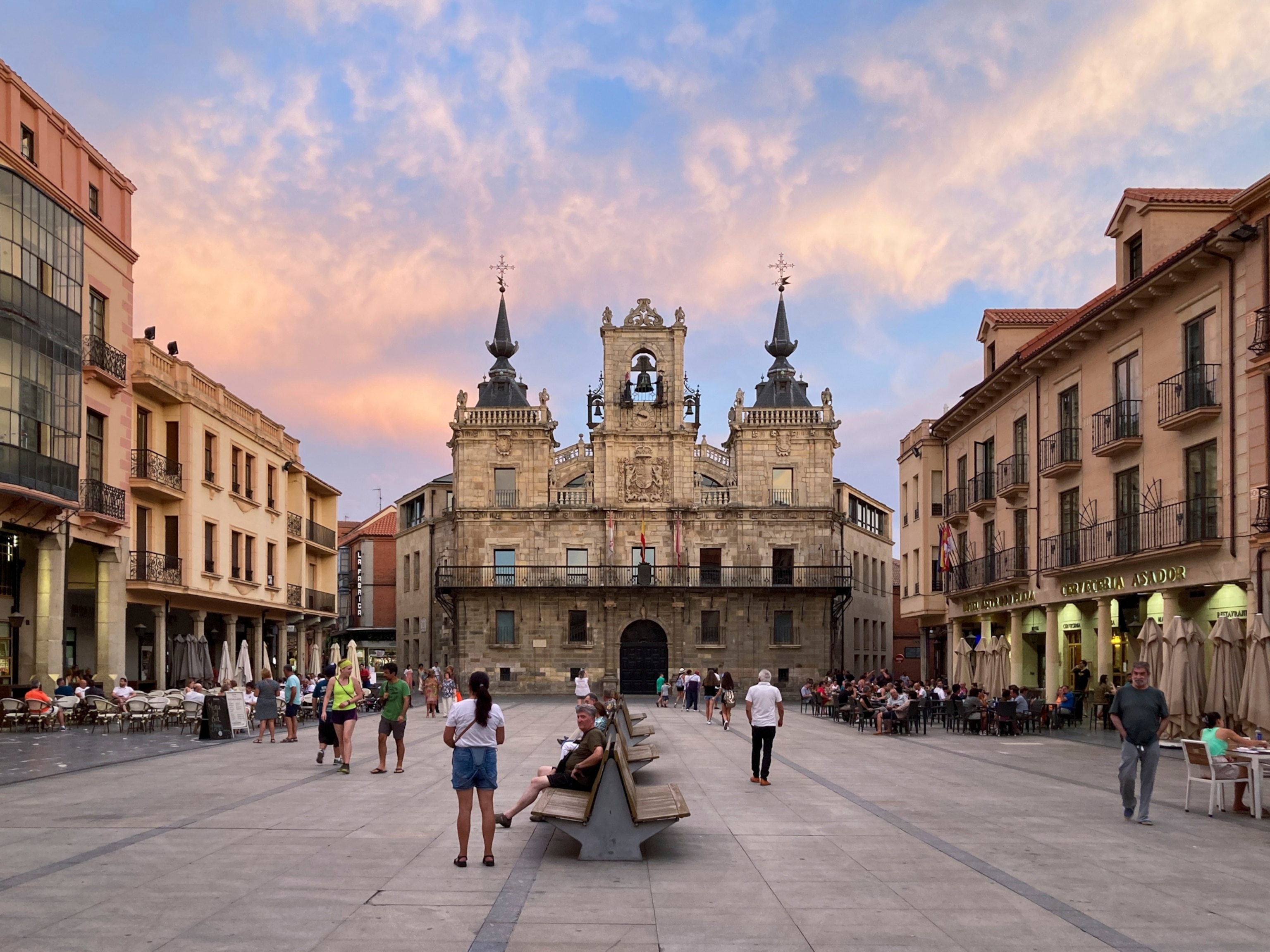 People in a plaza under a soft colorful sky.