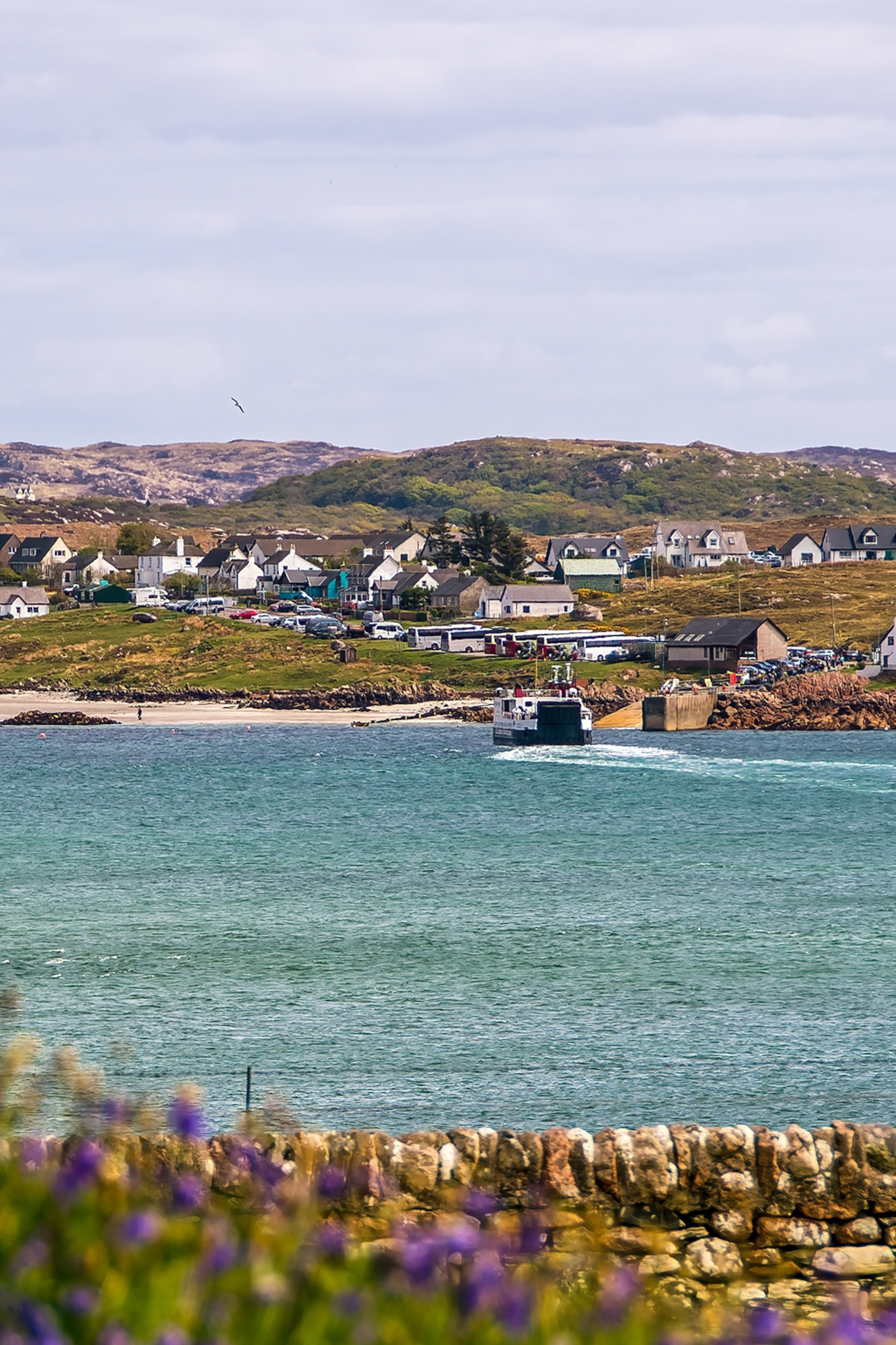 A calm coastline of an island in Scotland with a small town perched on the edge and a boat about to take off.