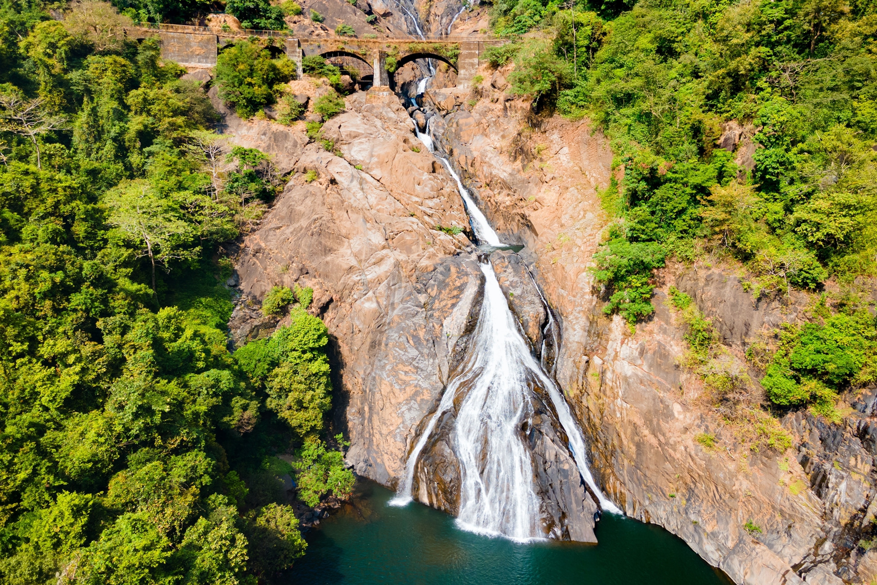 The side wall of a mountain with a waterfall running down into a lake and through a train viaduct.