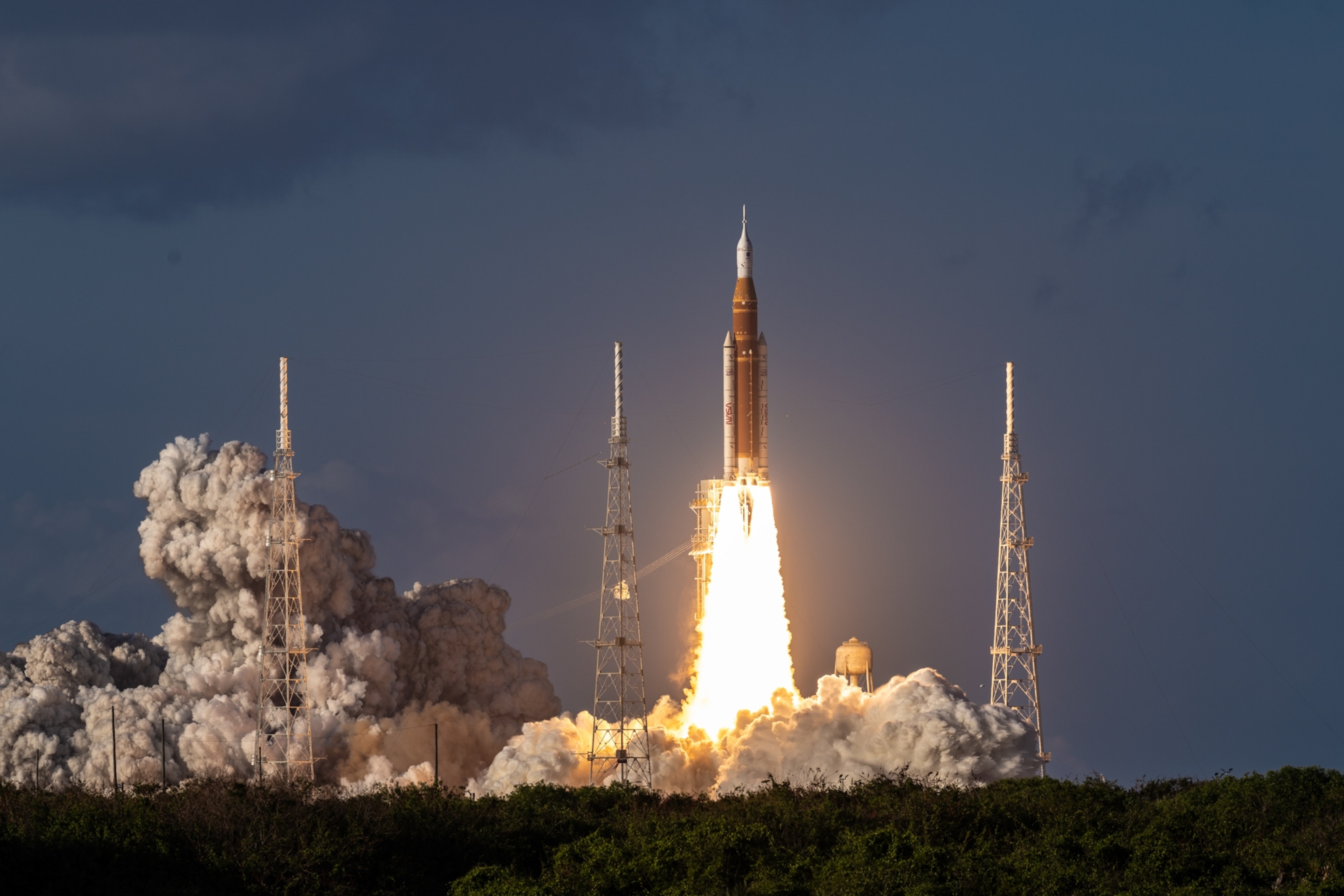 A rocket launches against a blue sky, emitting bright flames and thick smoke.