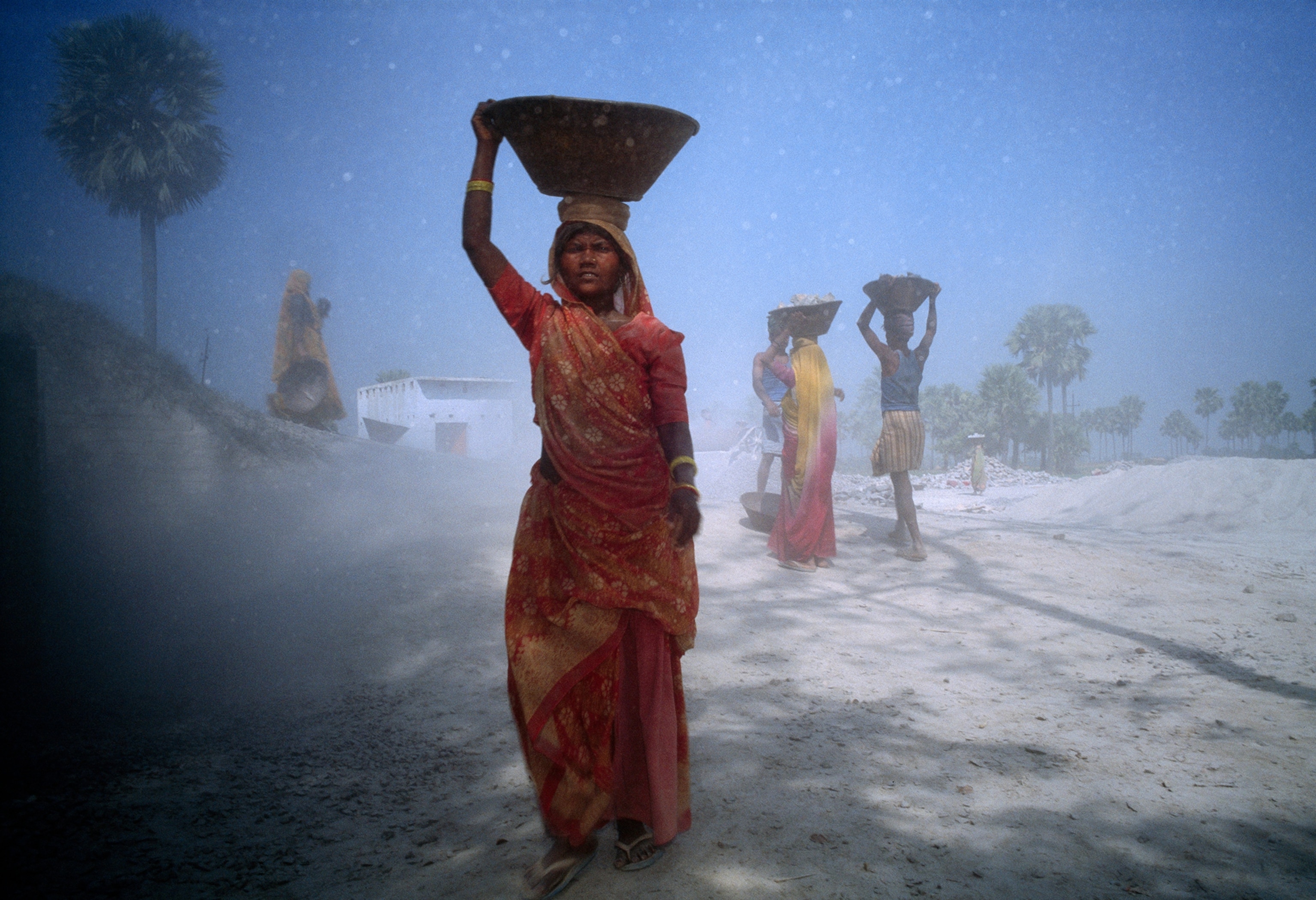 An Indian woman carries a tub of crushed rock upon her head.
