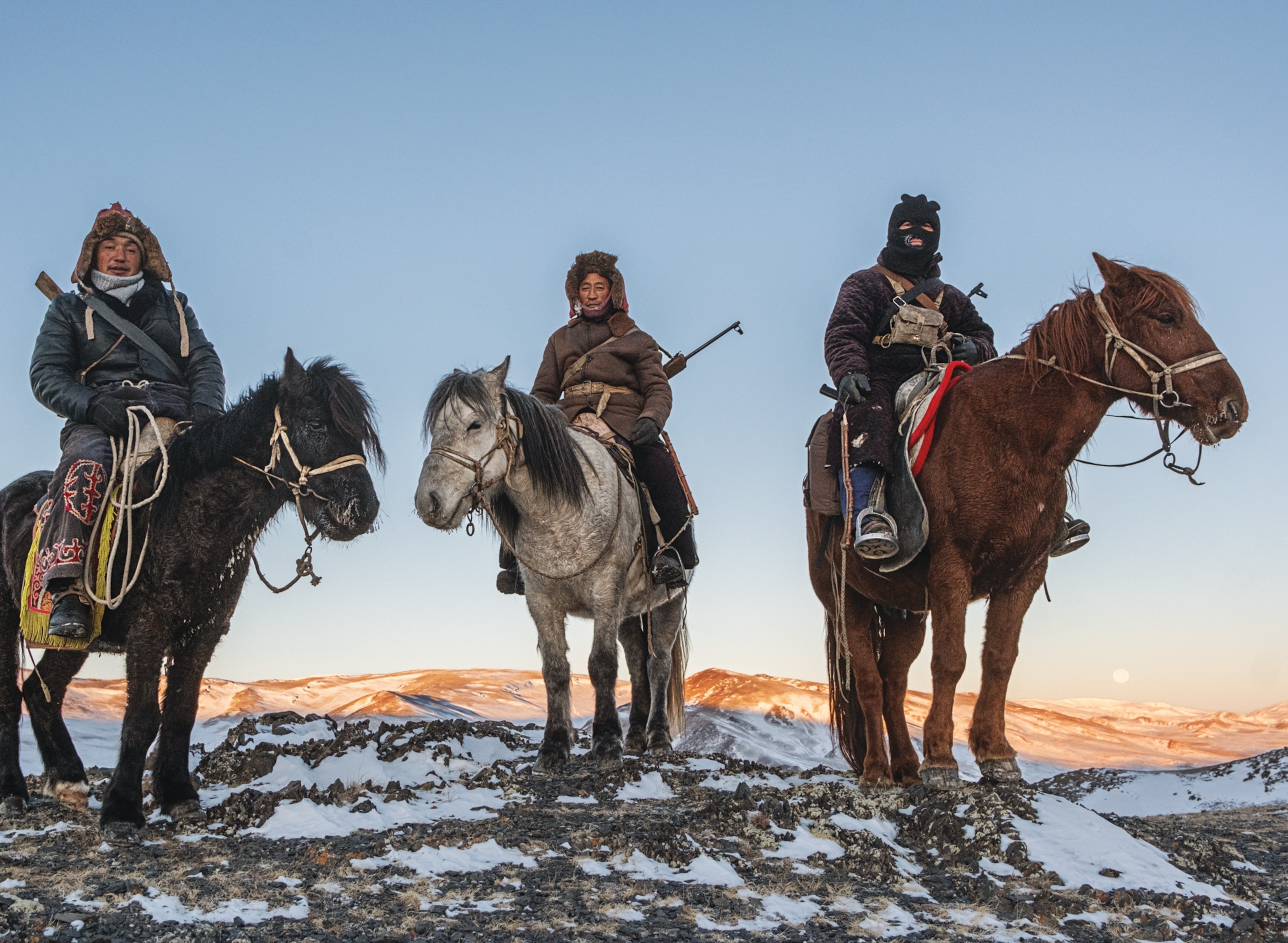 Three men with rifles on horses. One is in balaclava, and two other in traditional winter hats.