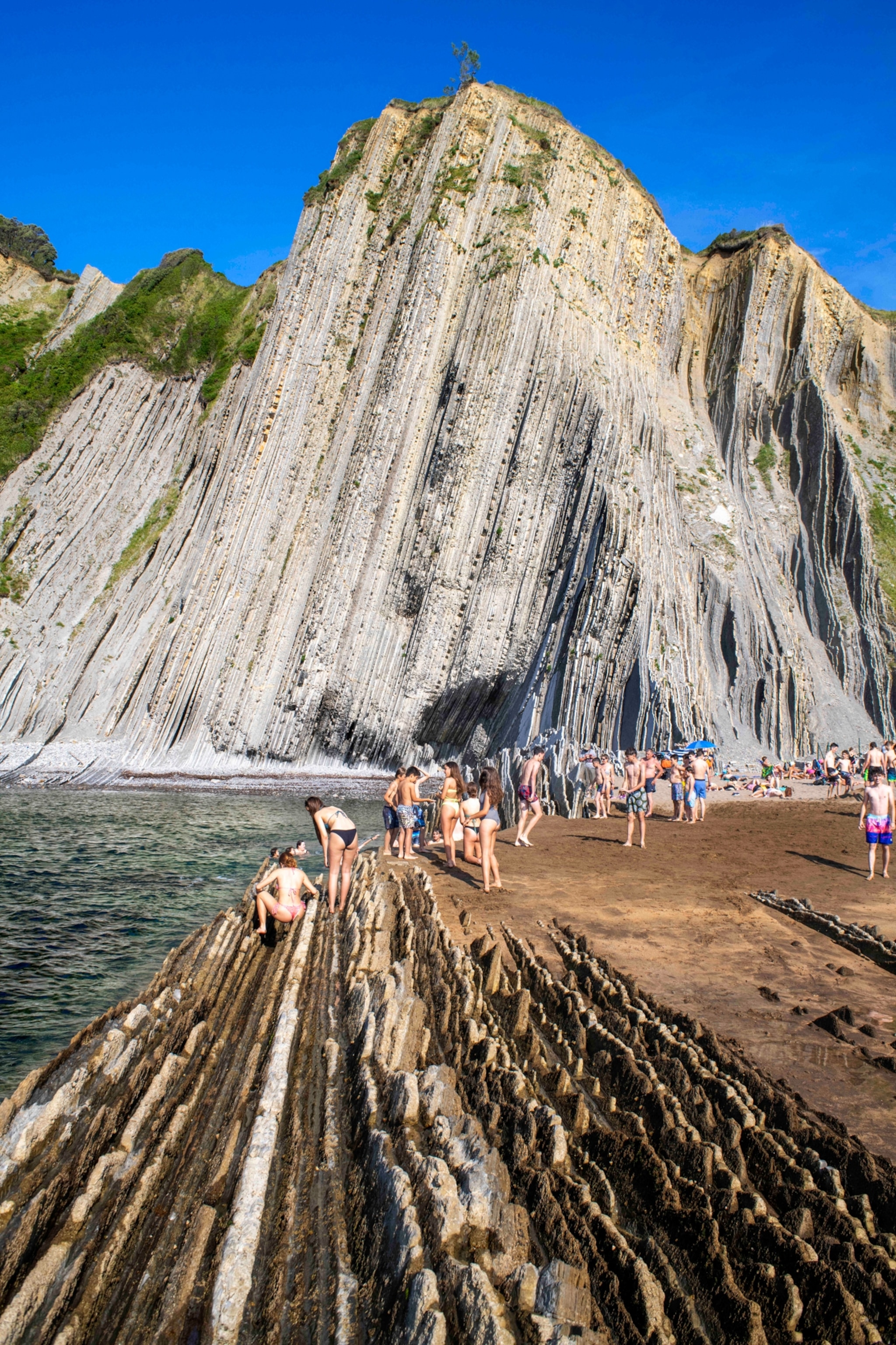 A group of people sit and stand on rock formations with a tall formation in the background.