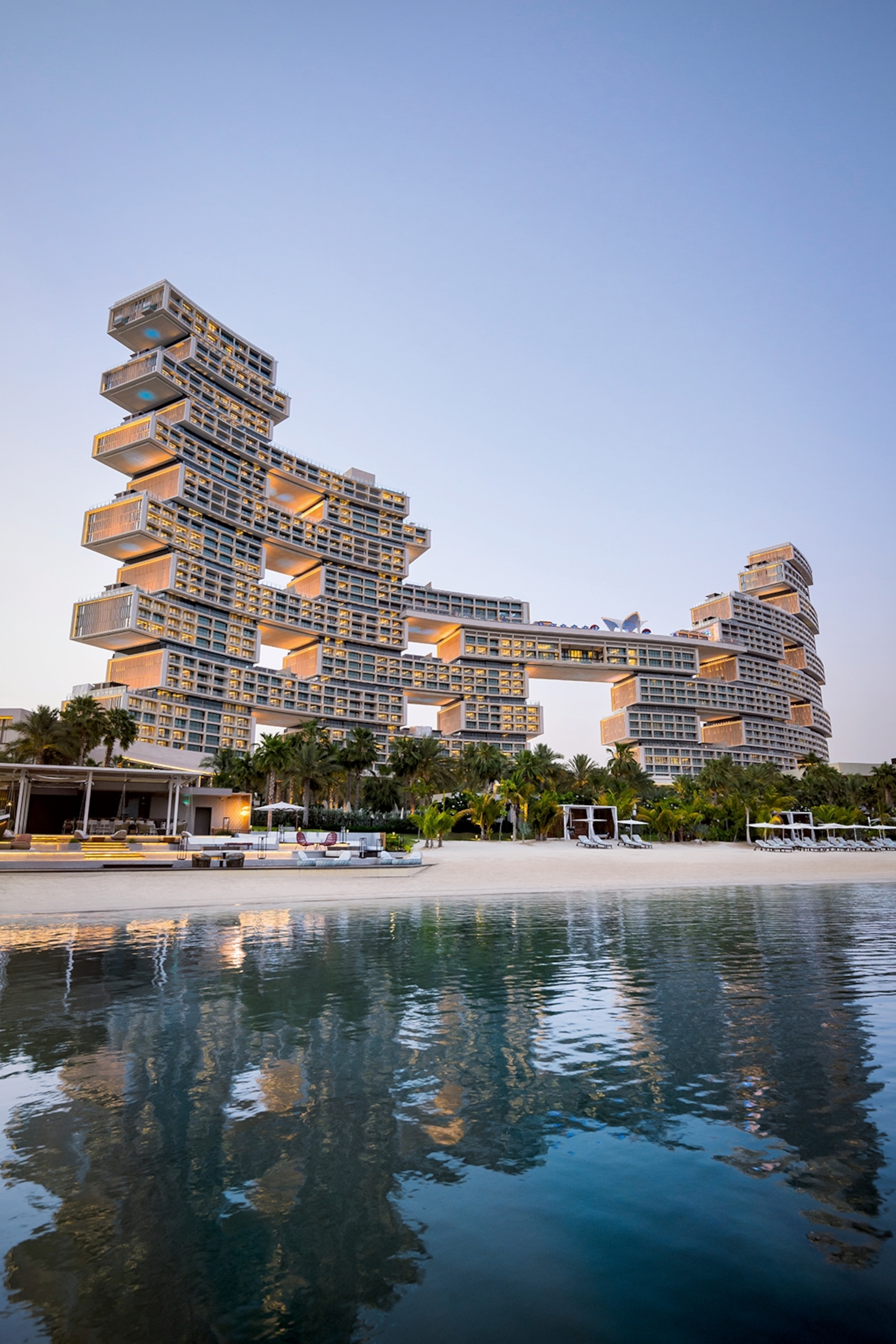 The exteriors of a tetris-like hotel seemingly built from room blocks on a palm-tree-lined waterfront.