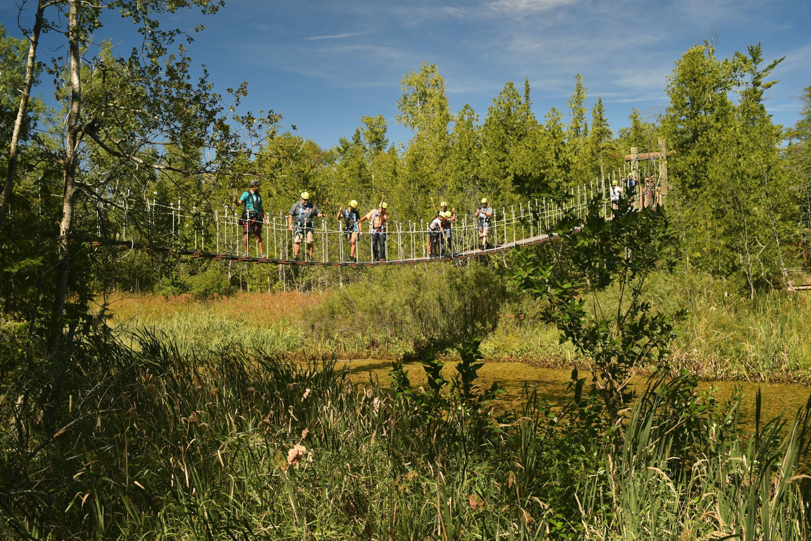 People crossing suspension bridge over pond with Lakeshore Adventures Zip Line Tours, Baileys Harbor, Door County, Wisconsin, USA