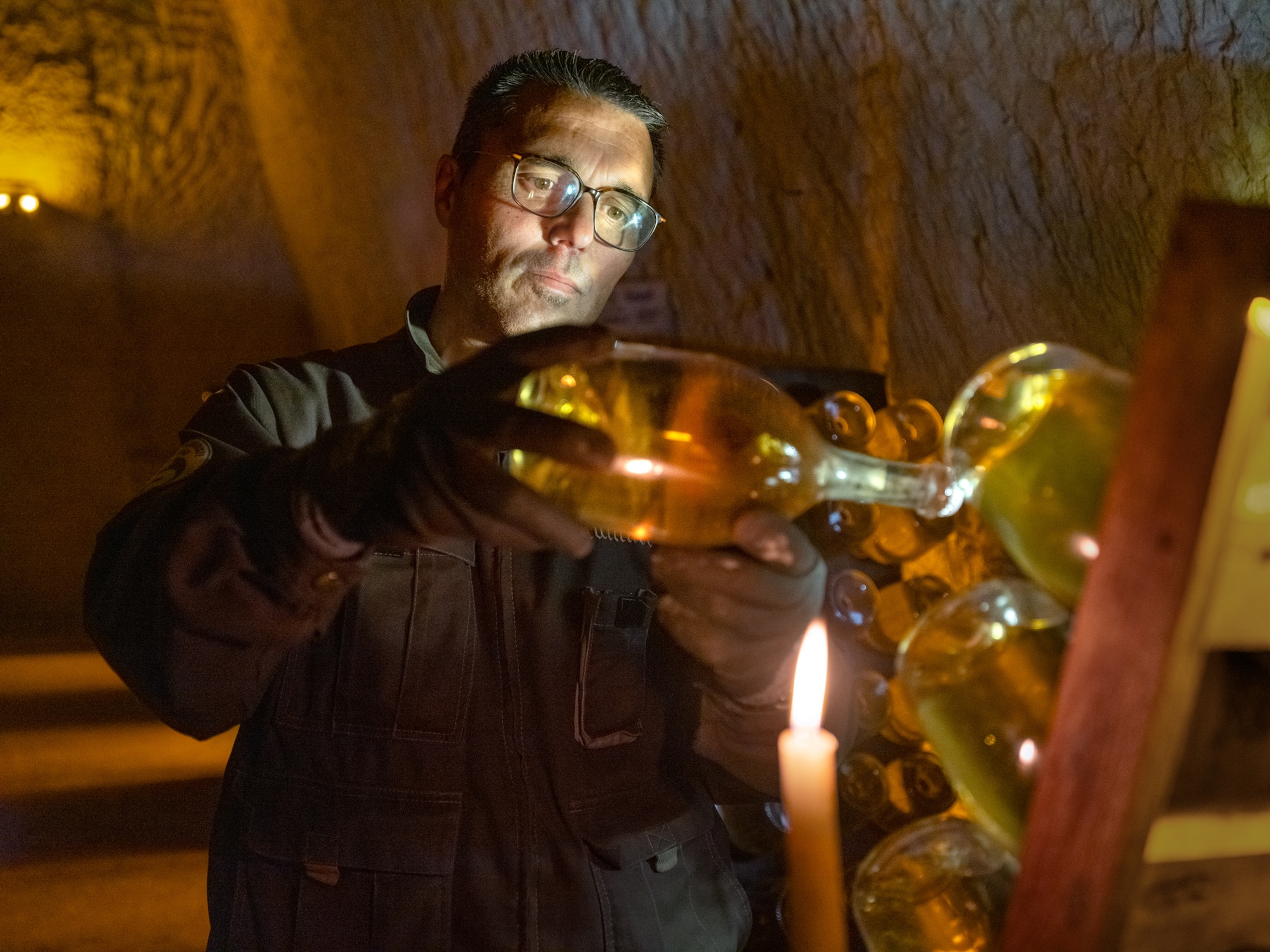 Pablo Lopez, a riddler at Ruinart, holds a bottle of white Champagne up to candlelight, carefully inspecting it for grape sediment as part of the riddling process prior to disgorgement.