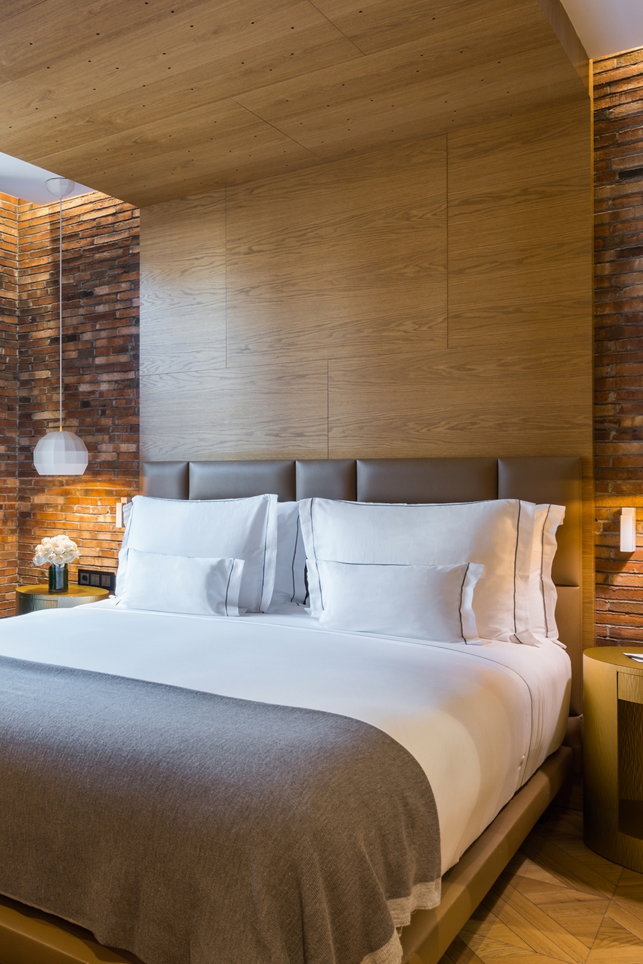 A modern double bedroom with a wooden headboard that reaches to the ceiling and slick brick walls.